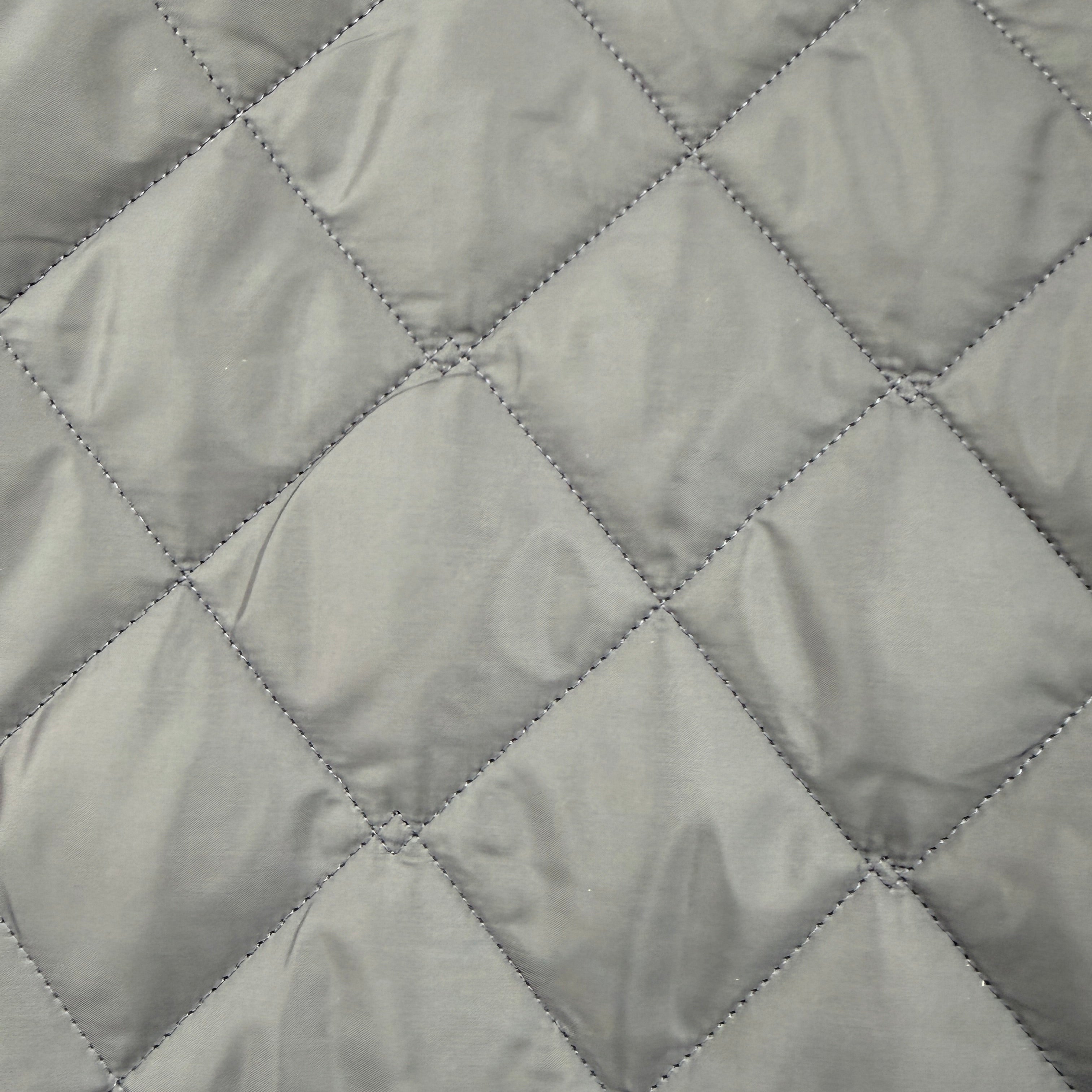Close-up of a light gray quilted fabric with a diamond pattern stitched by matching gray thread.