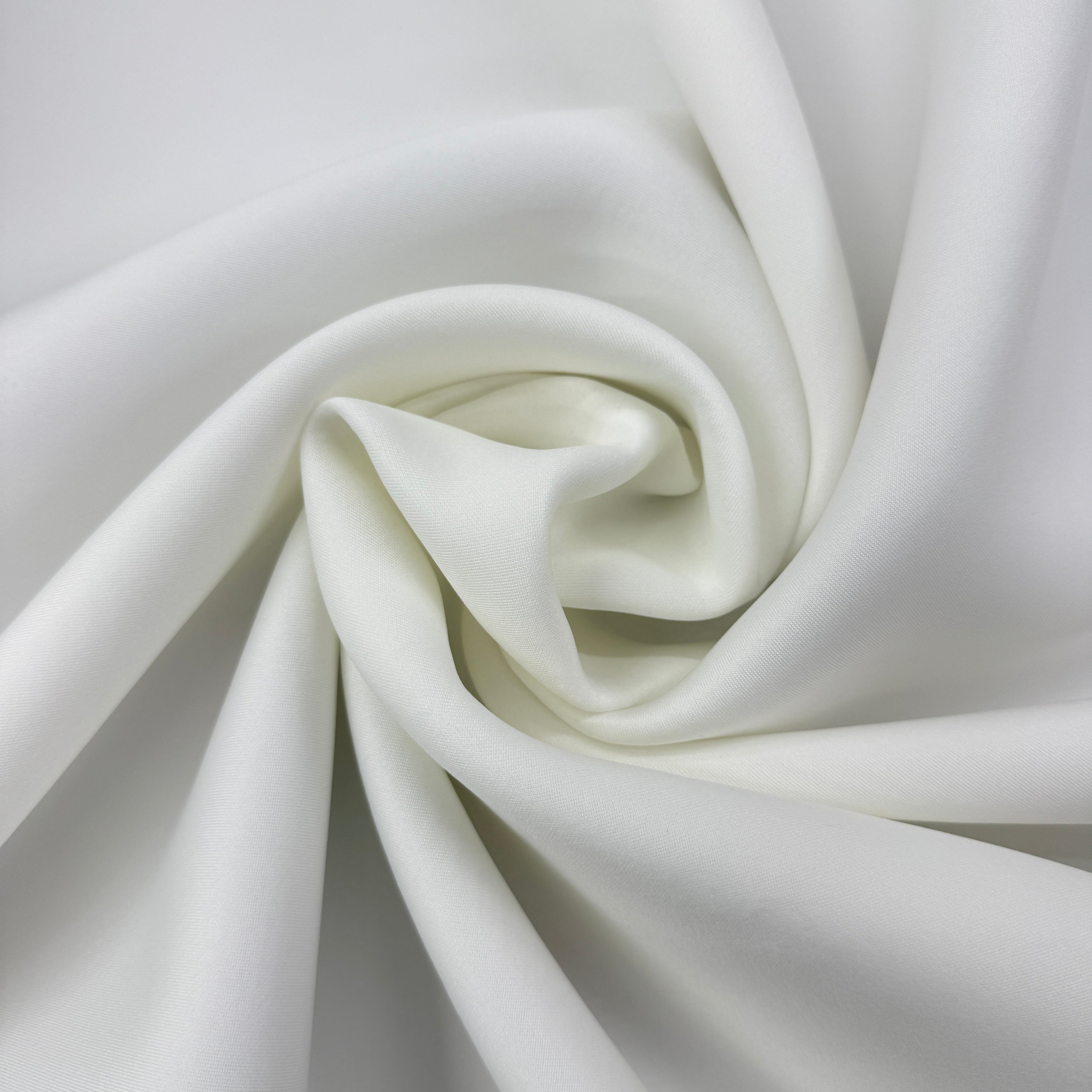 A close-up of white satin or silk fabric arranged in a spiral drape, showing its smooth texture and soft sheen.