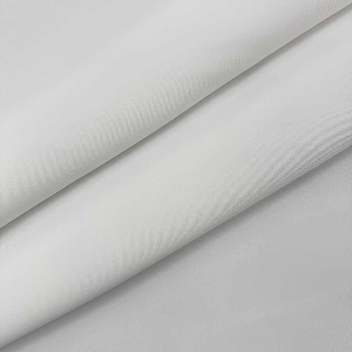 A close-up of a light gray fabric or material surface with soft diagonal folds and shadows.