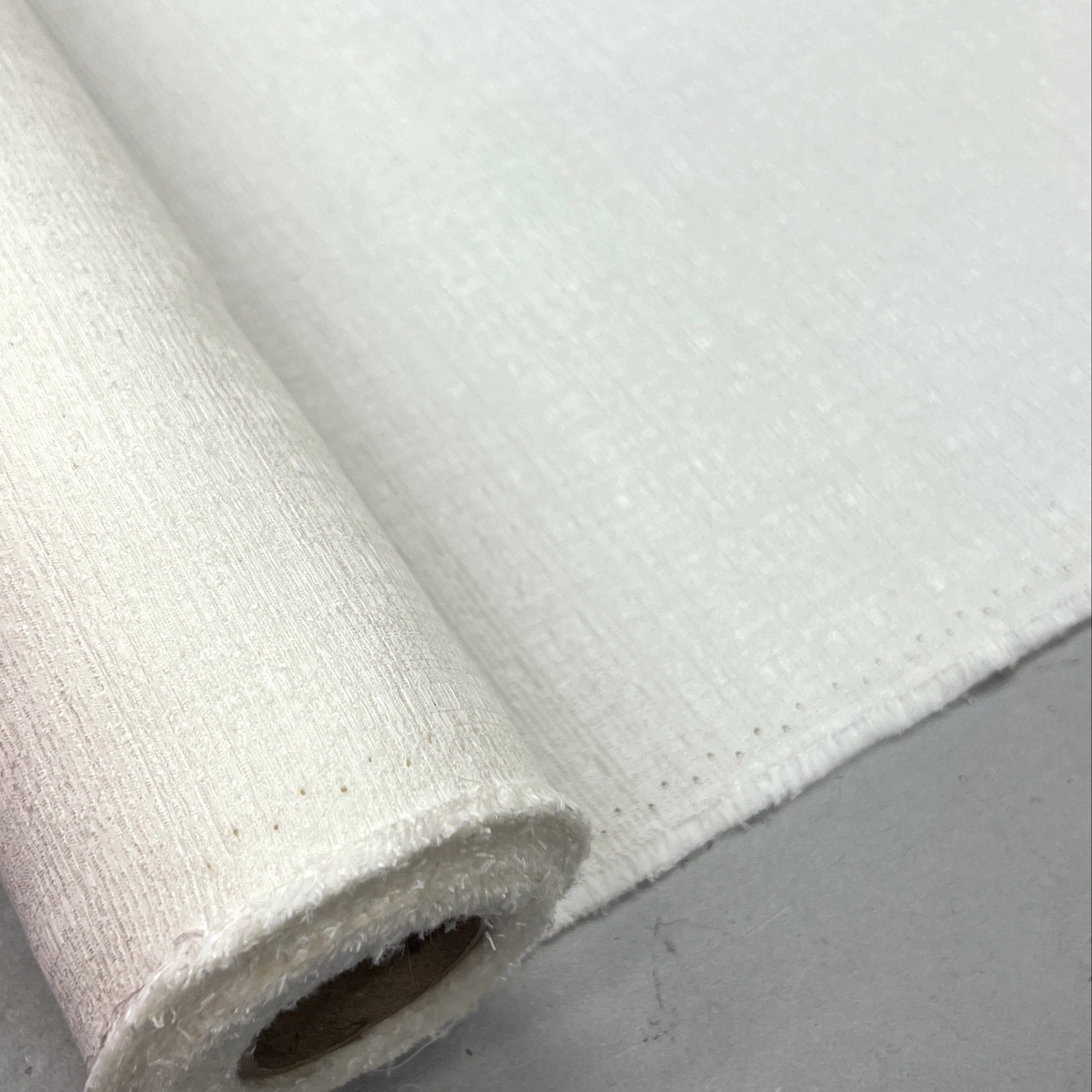 A close-up of a rolled white fabric or material sample laid on a gray surface.