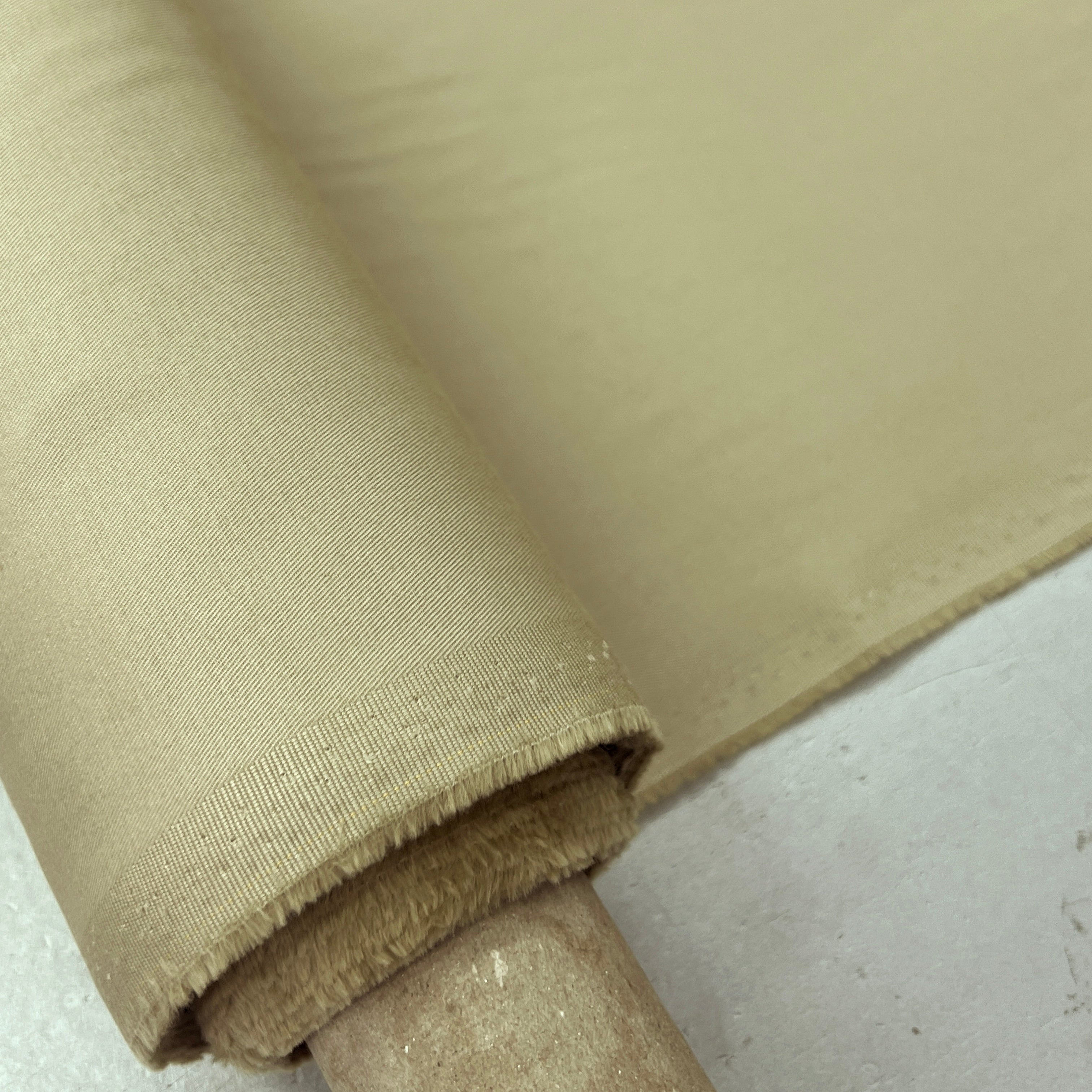 A close-up of a roll of beige fabric draped over a wooden spool, showing the woven texture and color of the material.