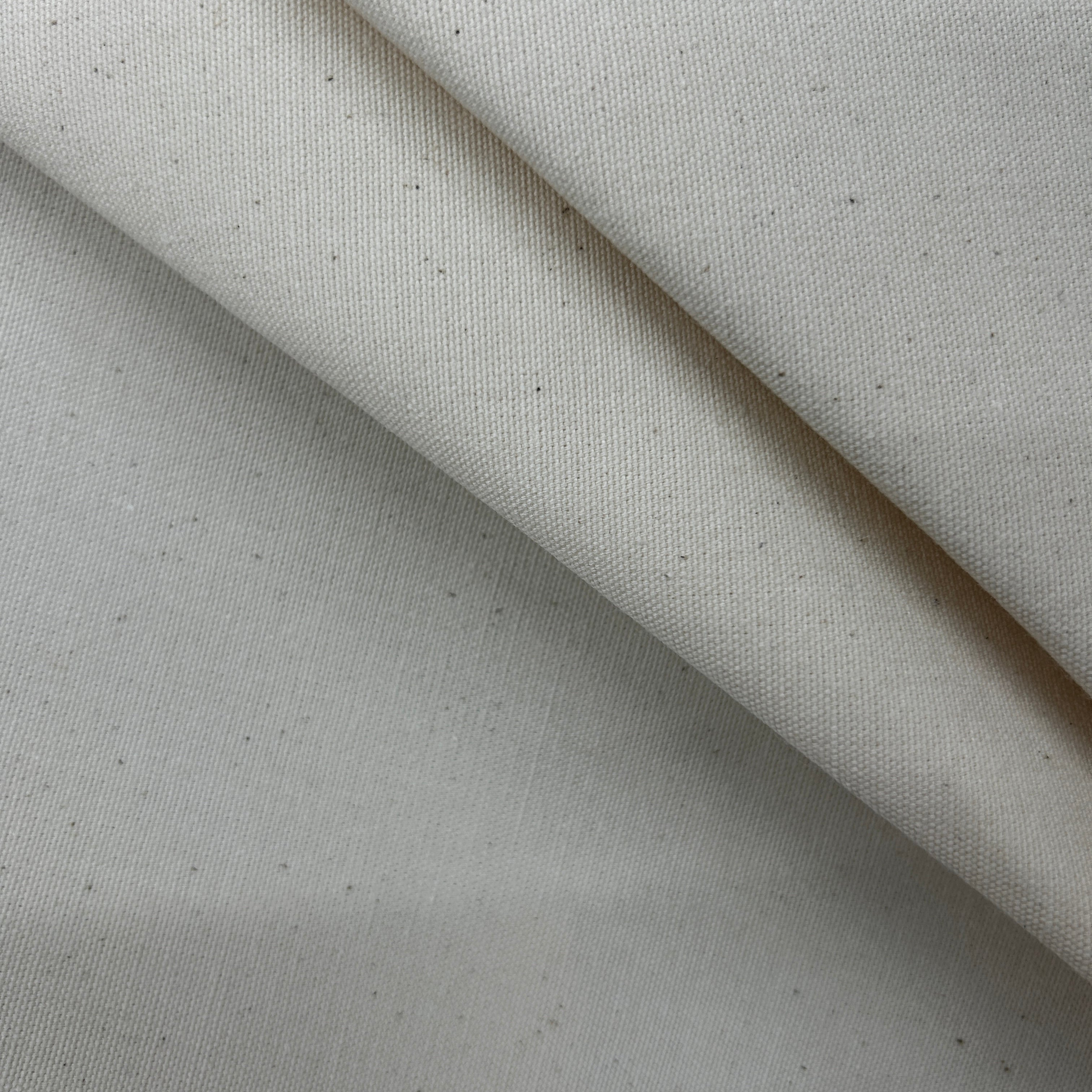 A close-up of a light beige fabric with a fine twill texture and small dark flecks, shown in soft diagonal folds.