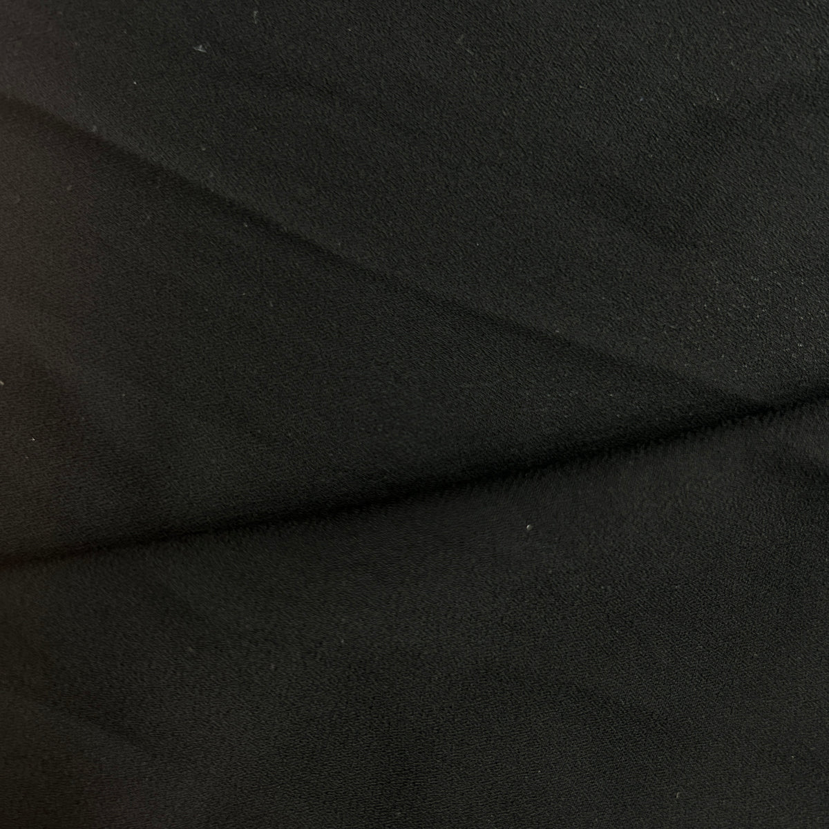 Close-up of black polyester double georgette crepe fabric showing its pebbled matte texture.