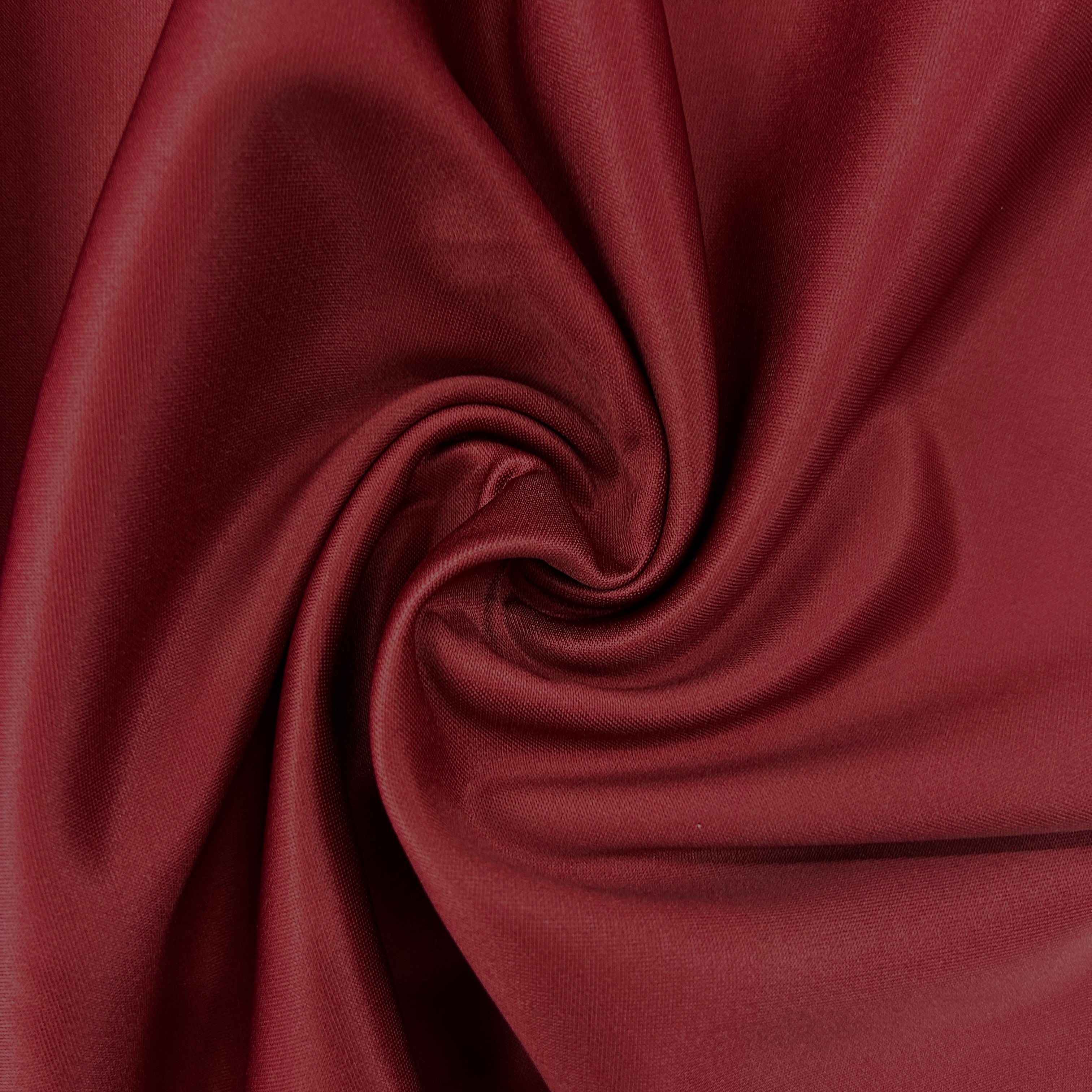 A close-up of draped burgundy fabric arranged in a spiral, showing its smooth texture and color.