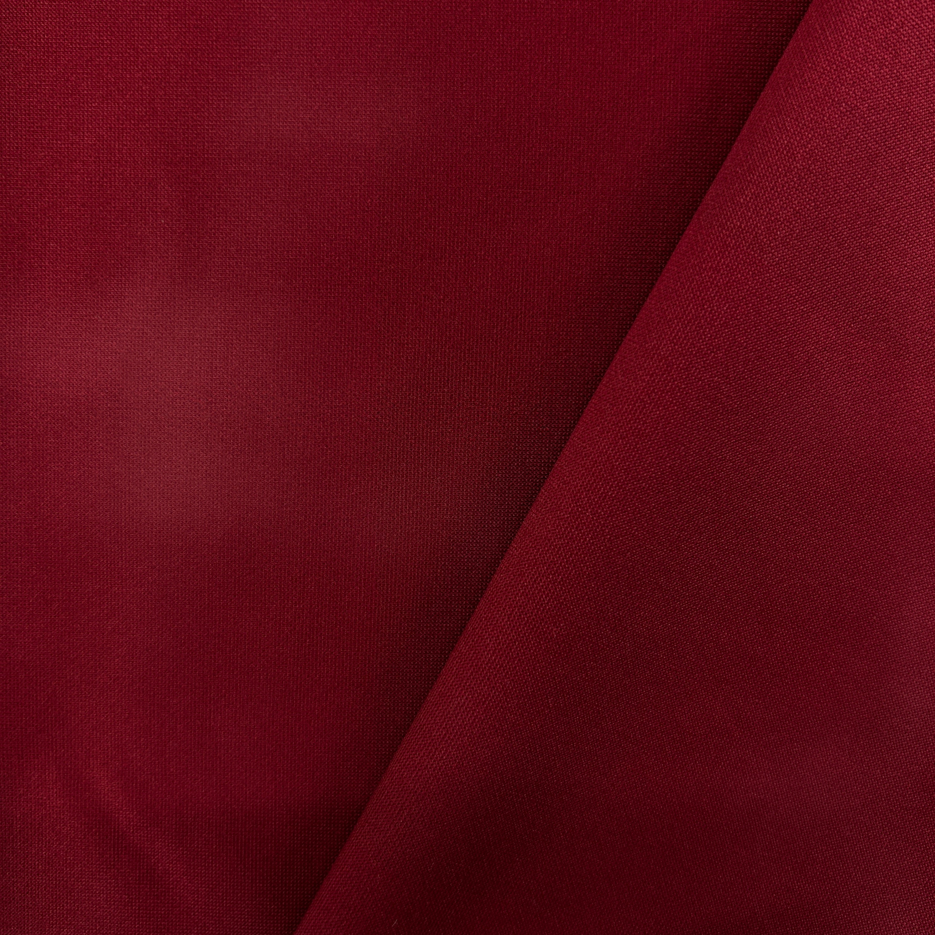 A close-up of deep burgundy fabric with a diagonal fold creating soft shadows, showing the material's fine texture.