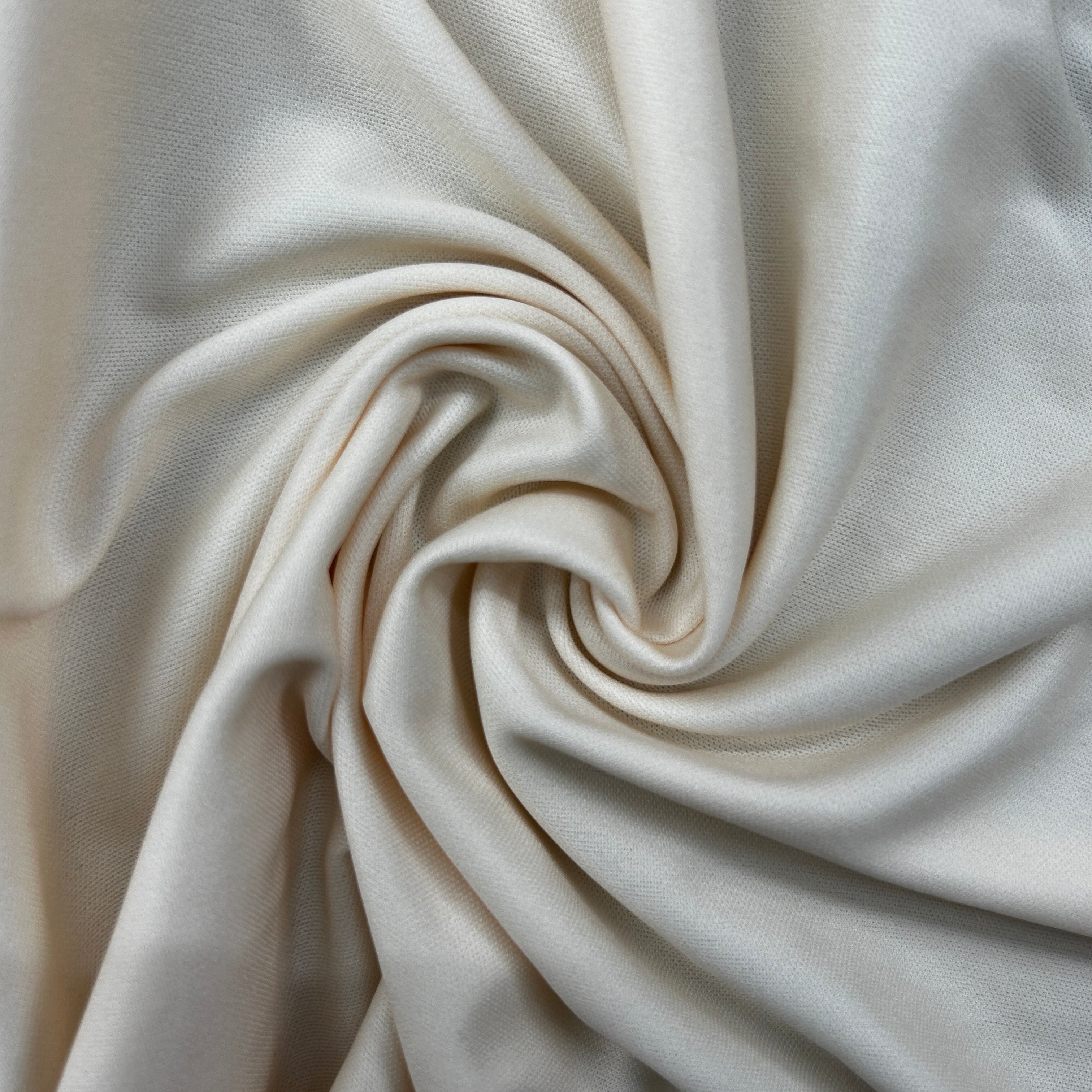A close-up of draped cream-colored fabric arranged in a spiral swirl, showing its soft texture and smooth surface.