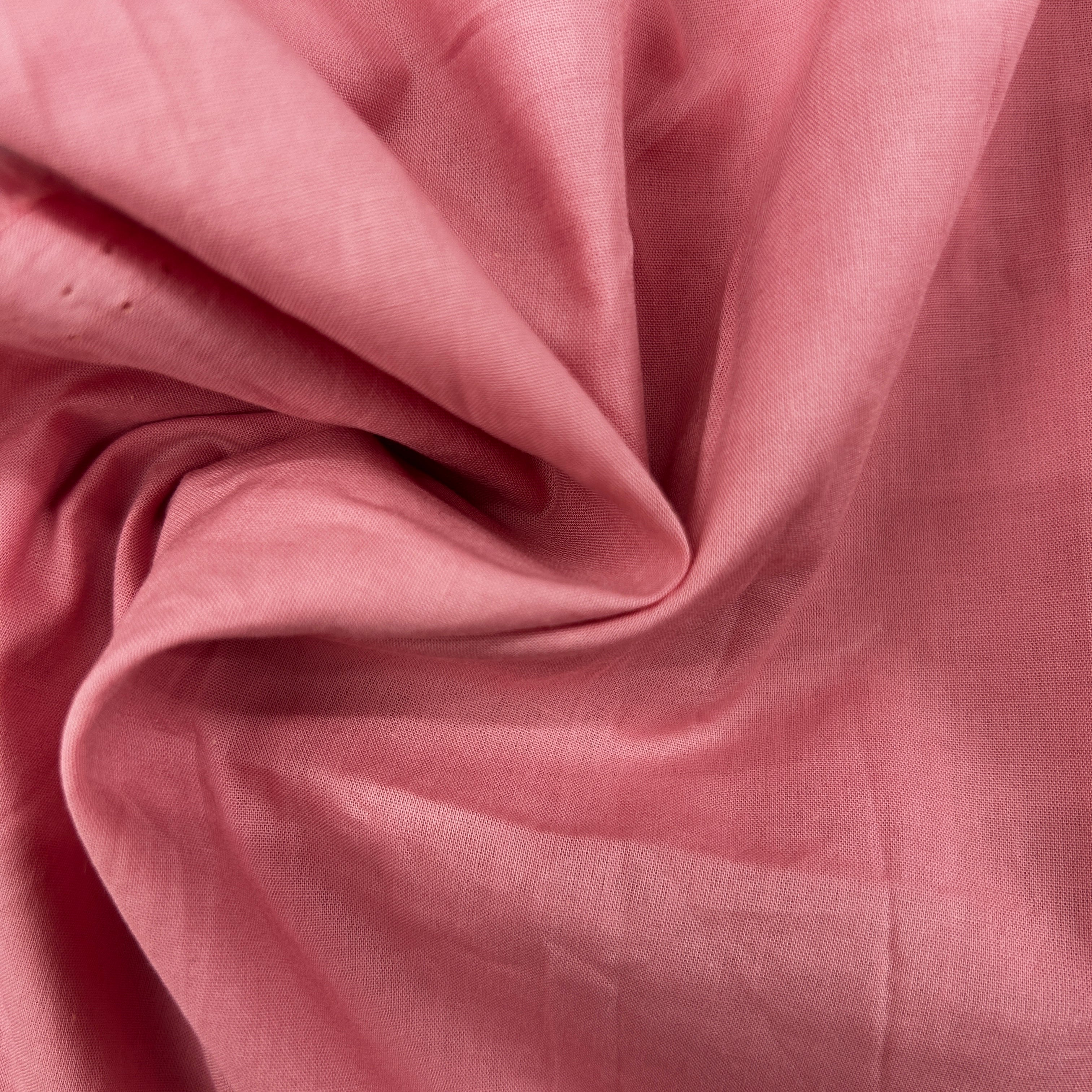 A close-up of draped dusty pink fabric with soft folds and a subtle woven texture.