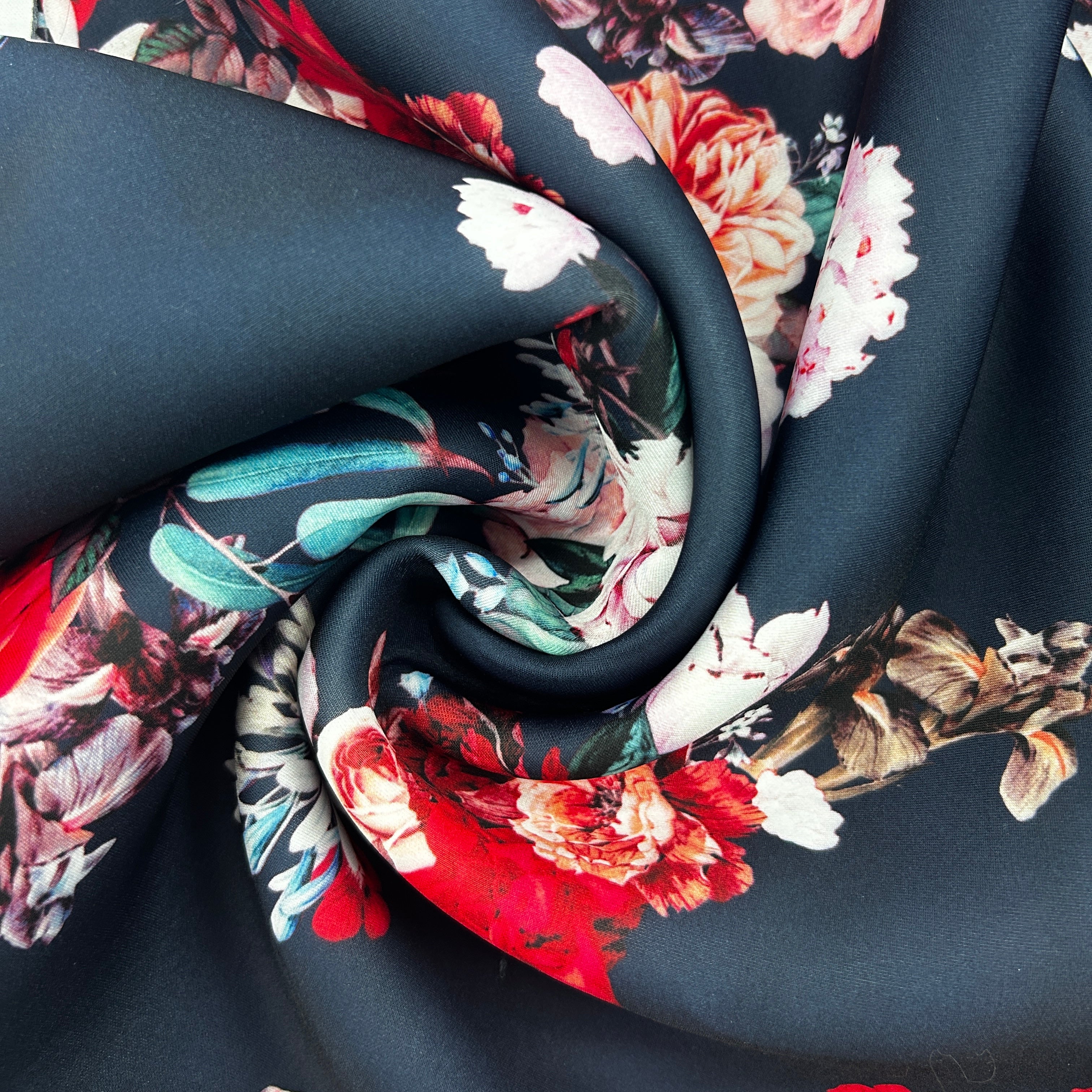 A close-up of draped fabric with a dark charcoal base and a large floral print in red, white, pink, teal, and brown.