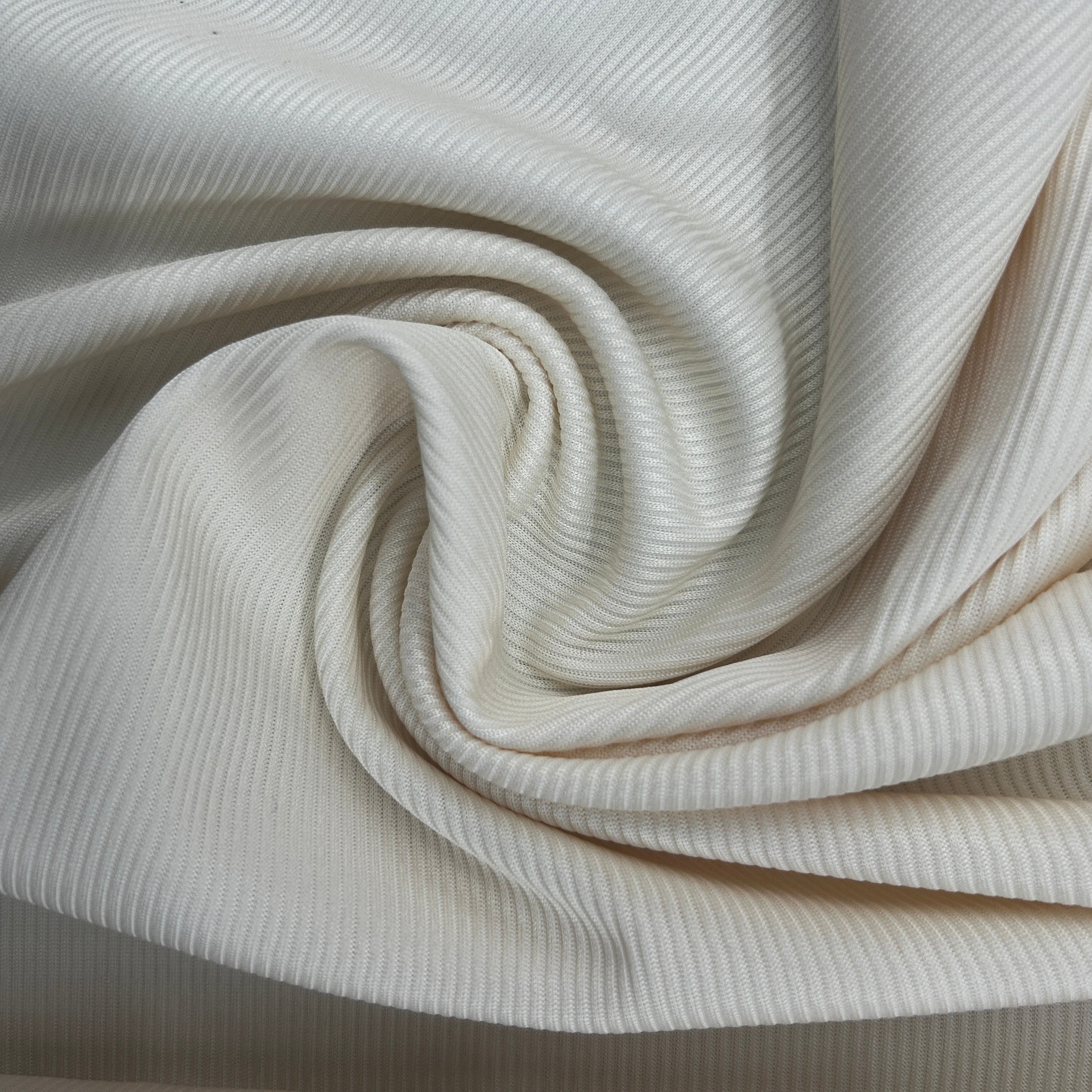A close-up of off-white ribbed fabric, likely jersey or jersey-like textile material, arranged in a spiral drape to show texture and color.