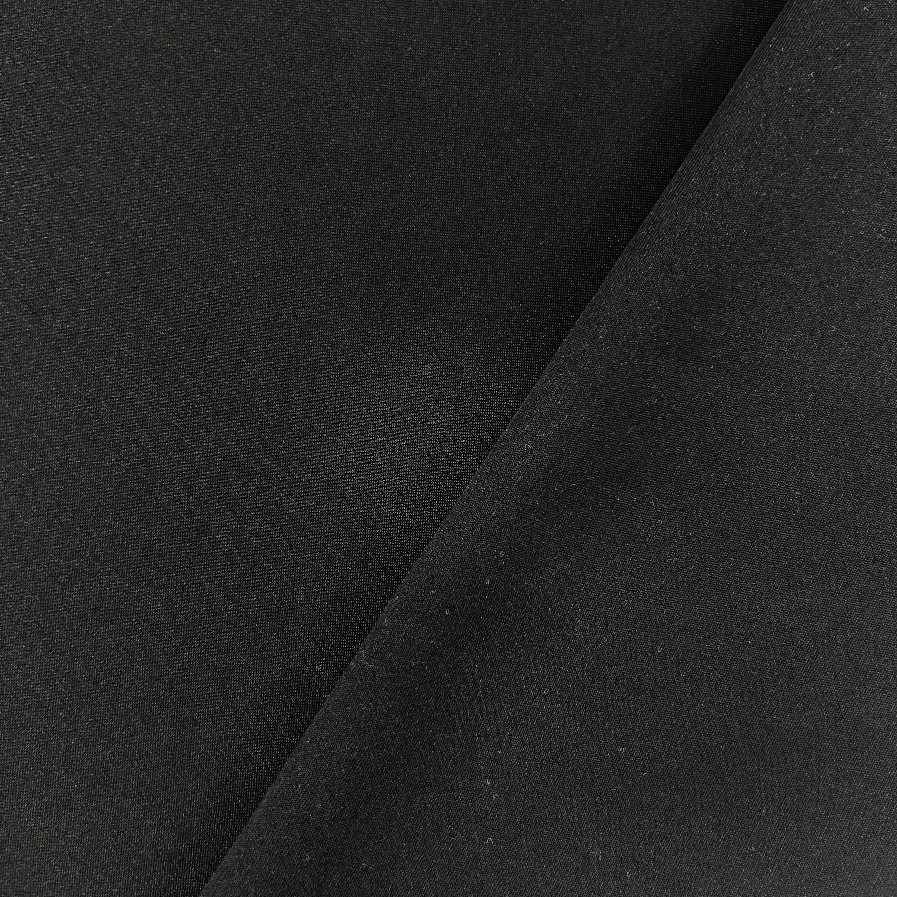 A close-up of black fabric with a diagonal fold creating a soft shadow across the surface.