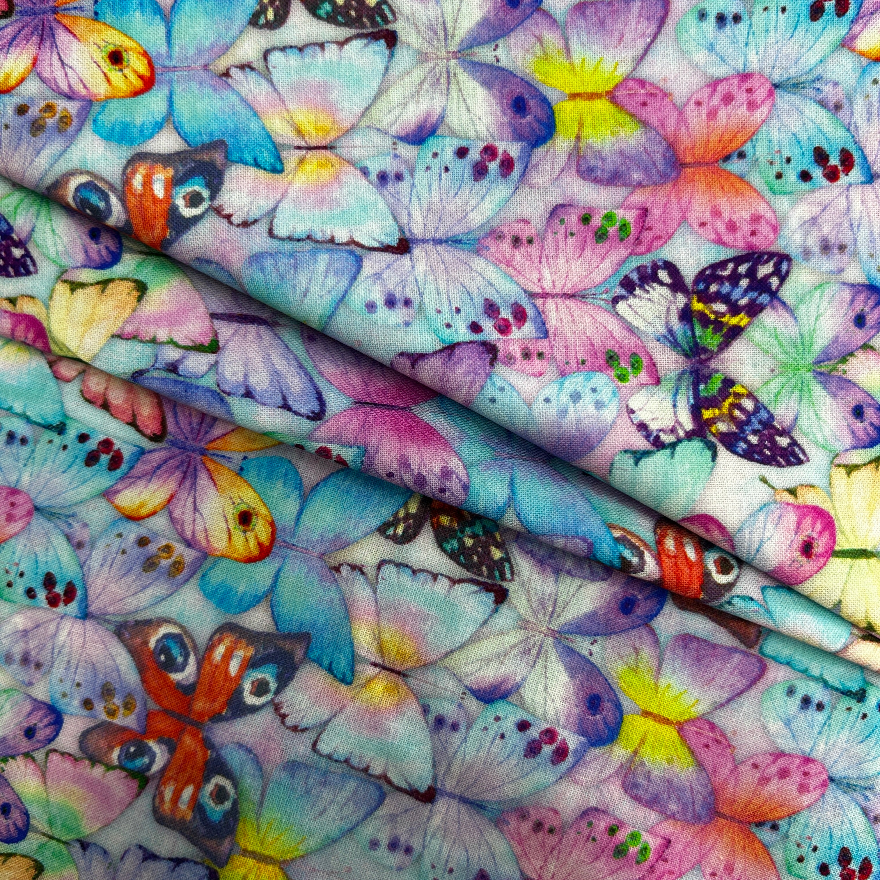 A close-up of a folded fabric featuring a dense, colorful butterfly print with pastel blue, purple, pink, yellow, and orange butterflies on a white background.
