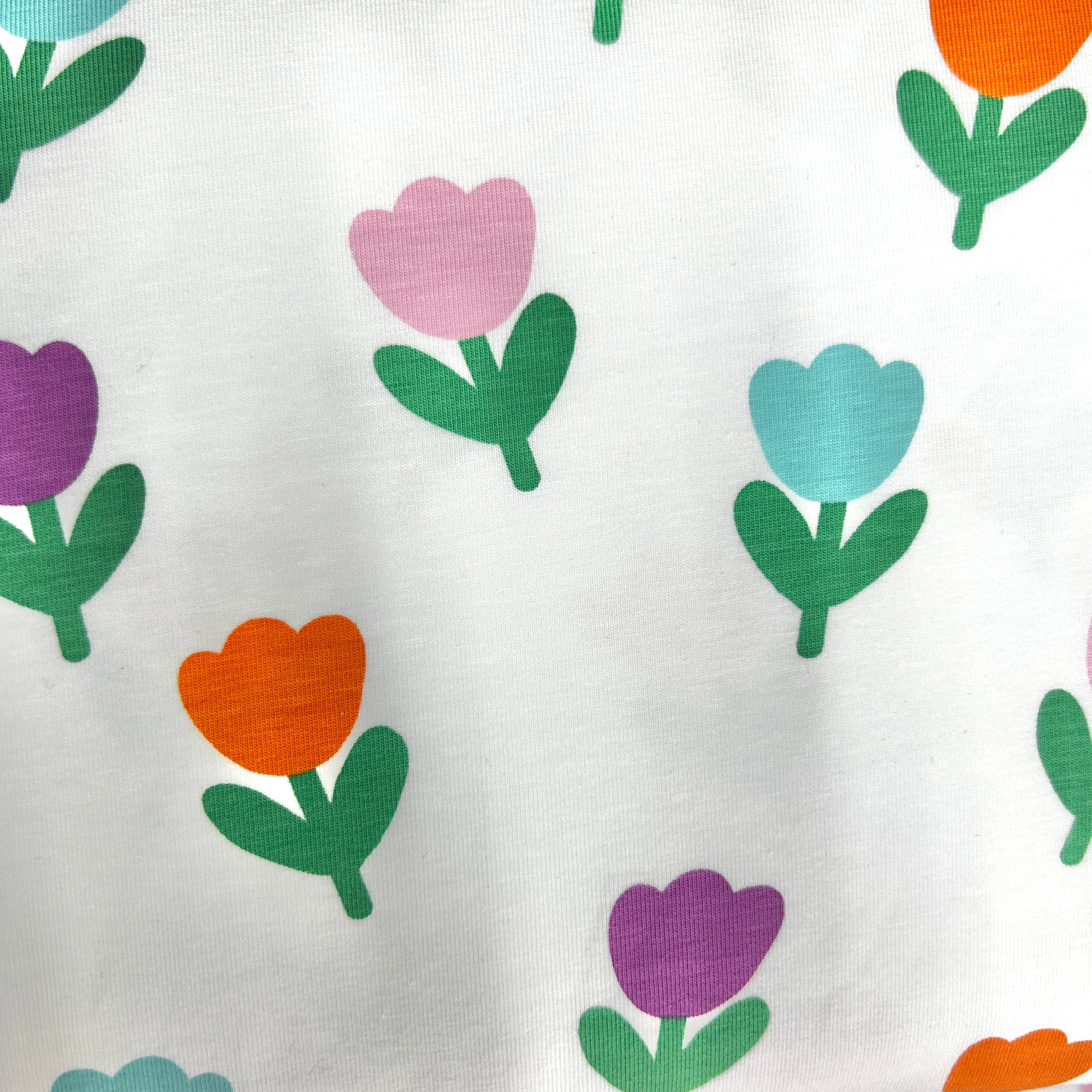 White fabric with a repeating pattern of stylized tulips in purple, orange, and light blue with green stems and leaves.
