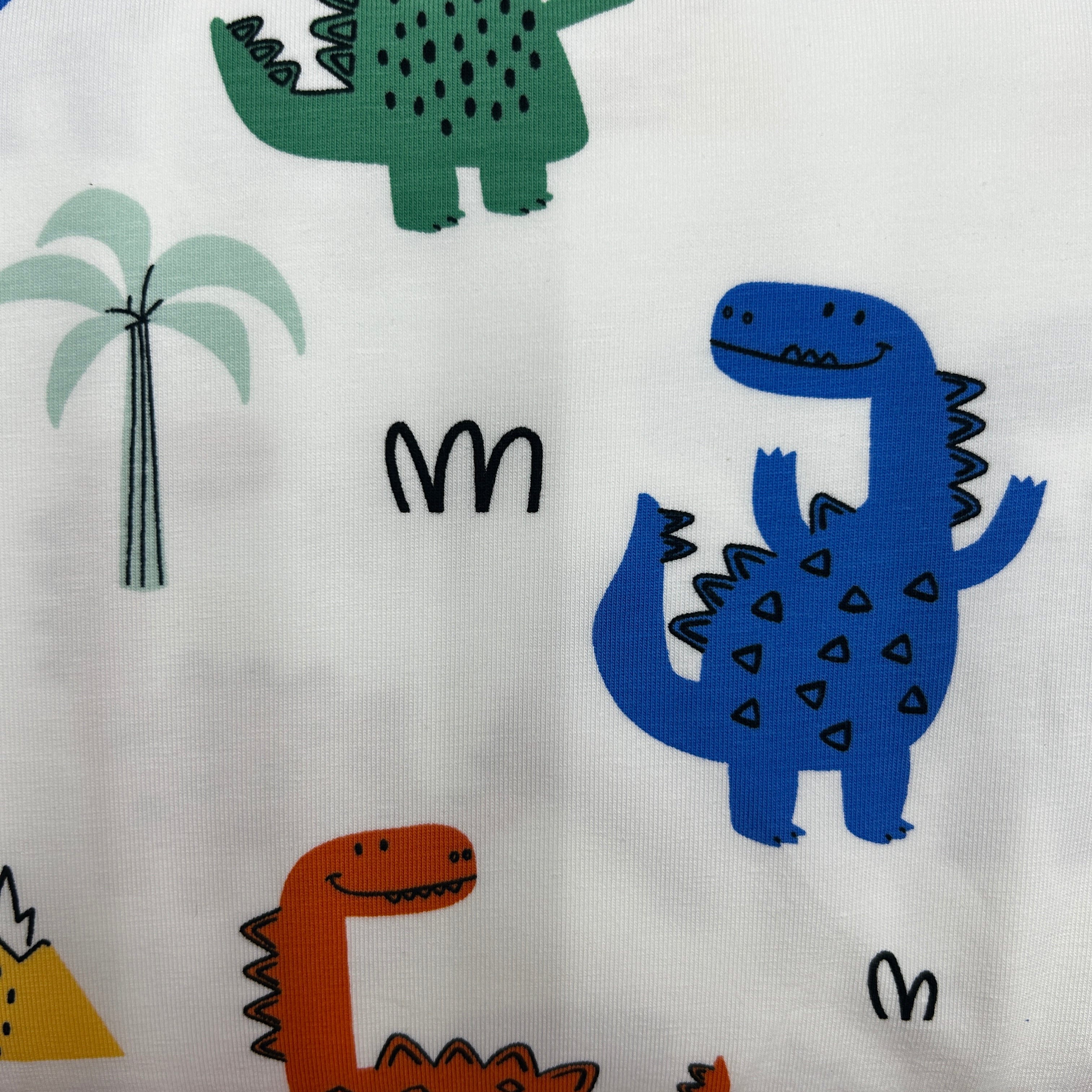 White fabric with a playful pattern of cartoon dinosaurs in blue, green, and orange, a palm tree, and small black letter-like shapes.
