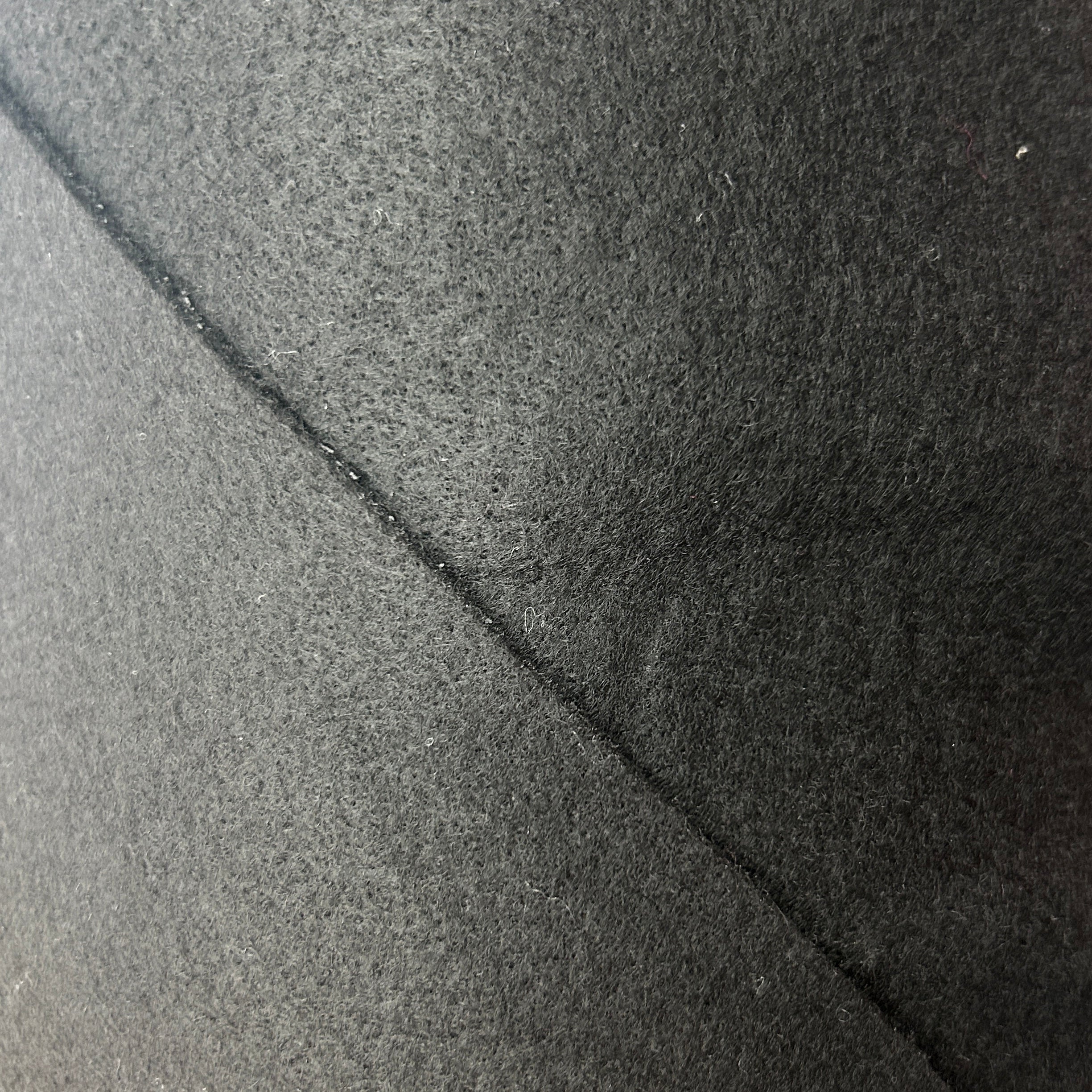 A close-up texture shot of a dark charcoal gray felt or fleece material, showing a diagonal seam.