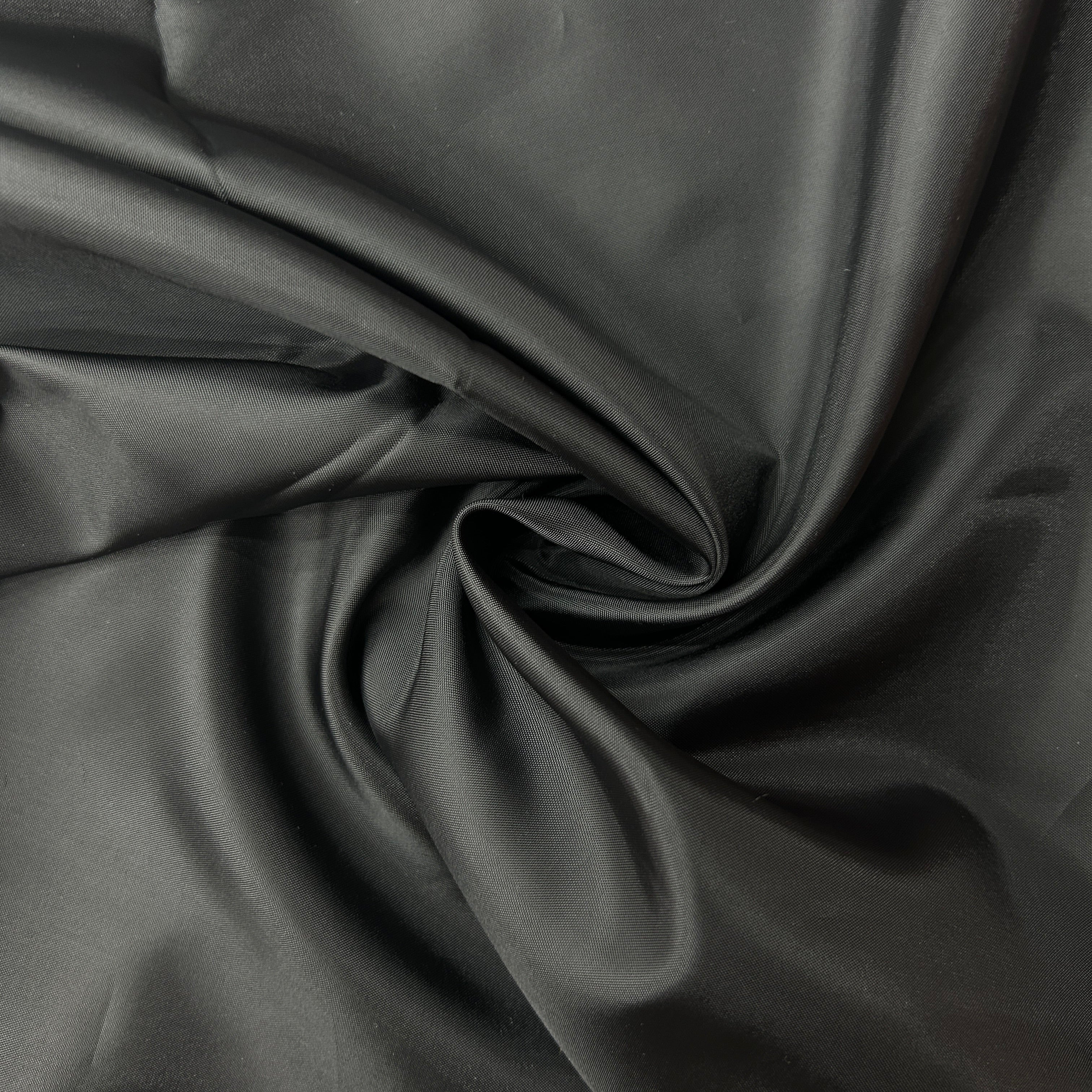 A close-up of draped black fabric with a smooth, slightly glossy texture arranged in soft folds and swirls.