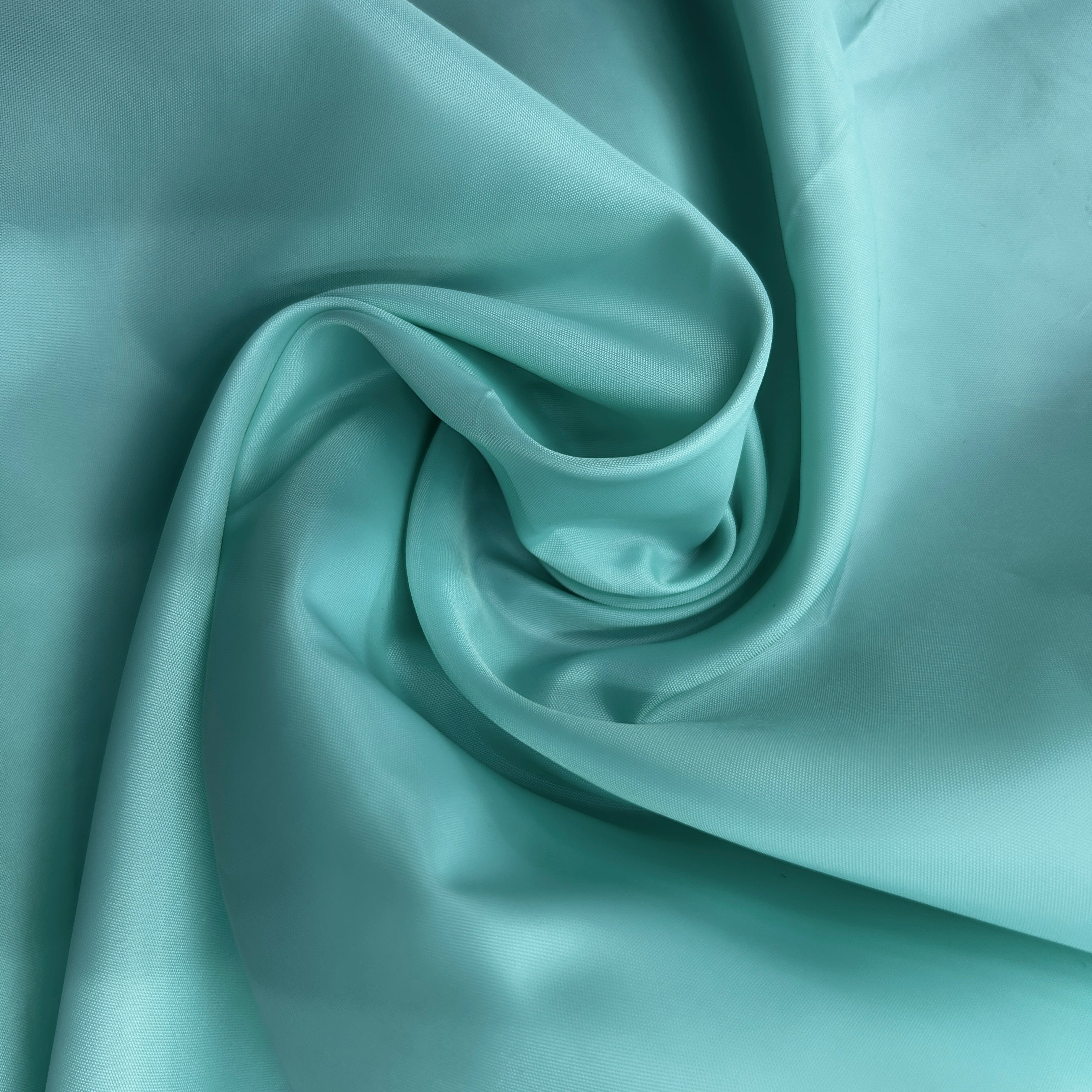 A close-up of draped mint green fabric with a smooth, satin-like sheen, arranged in a central swirl.