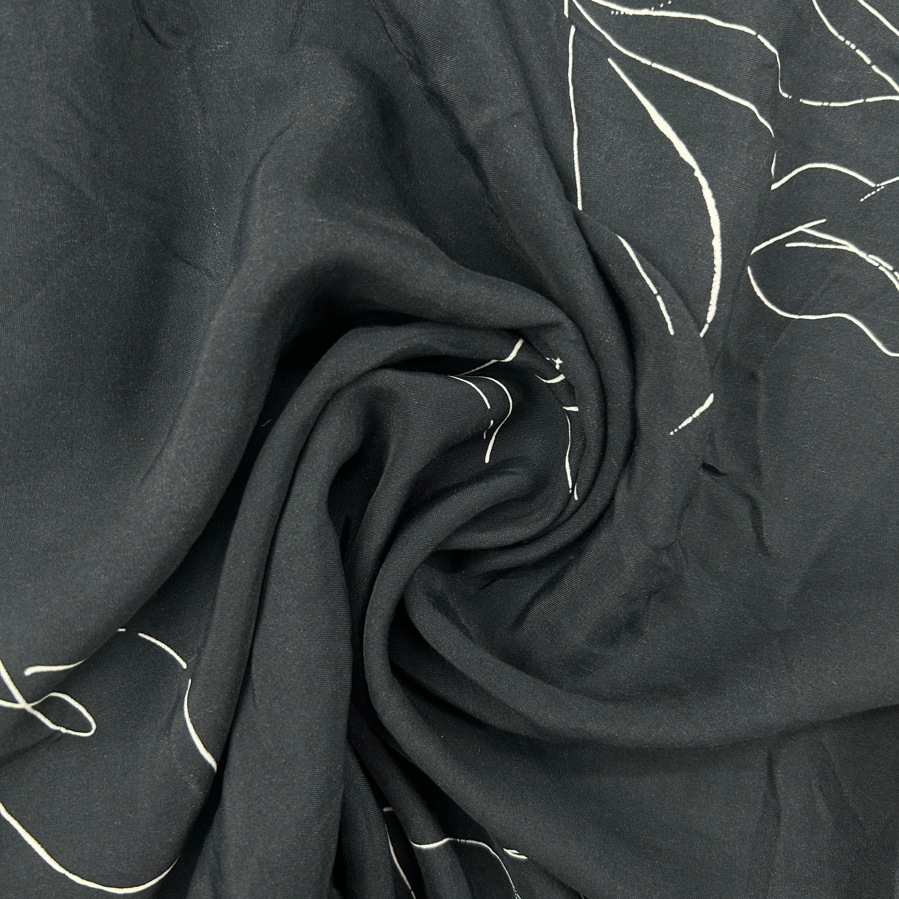 Black fabric with a white abstract line pattern, draped in a spiral to show texture and pattern detail.
