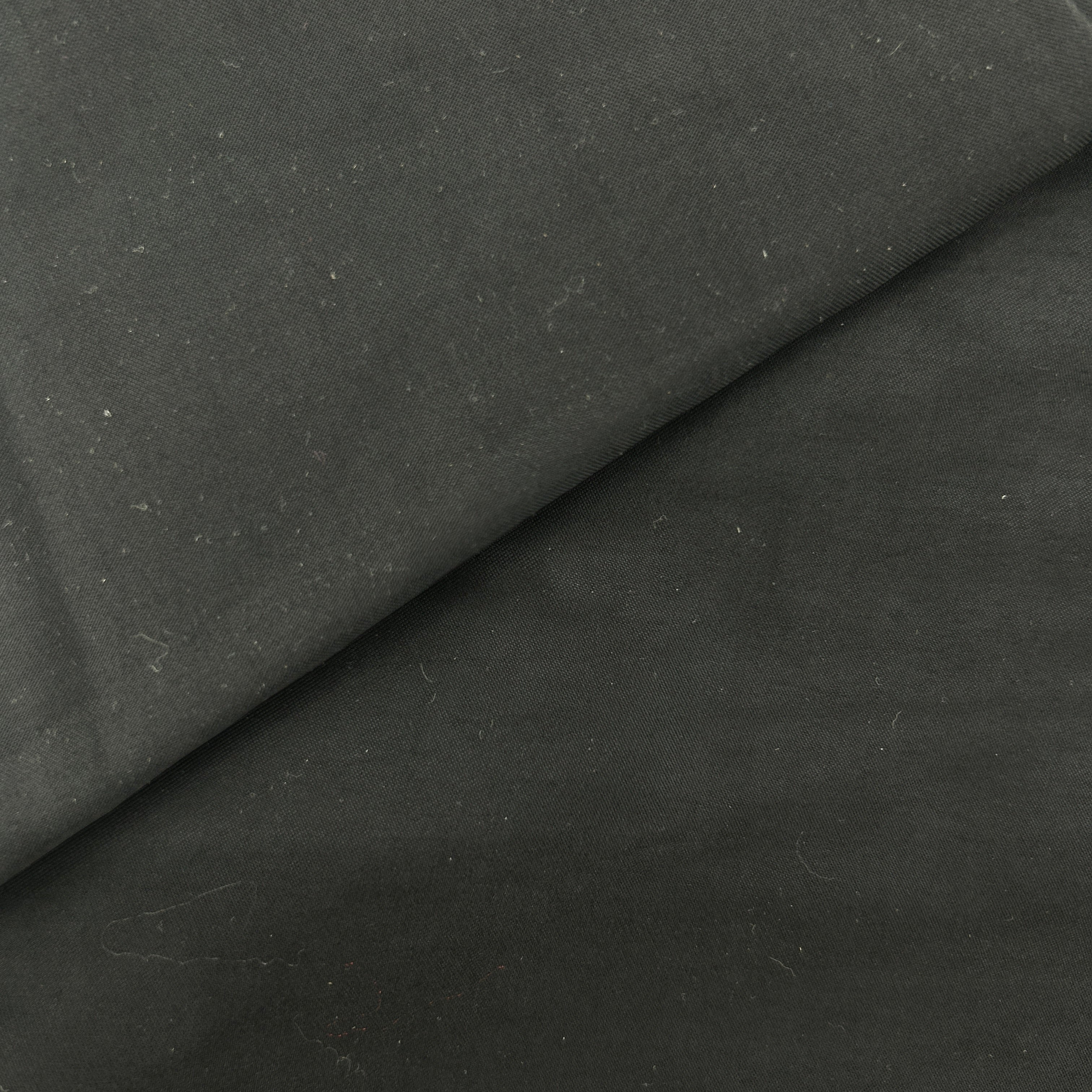 A close-up of dark charcoal gray fabric with a soft diagonal fold showing its texture and matte finish.