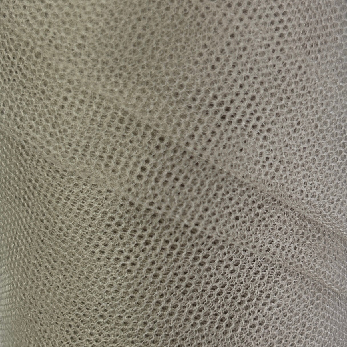 A close-up of a light gray or off-white mesh fabric with a fine, repeating perforated pattern and soft folds.