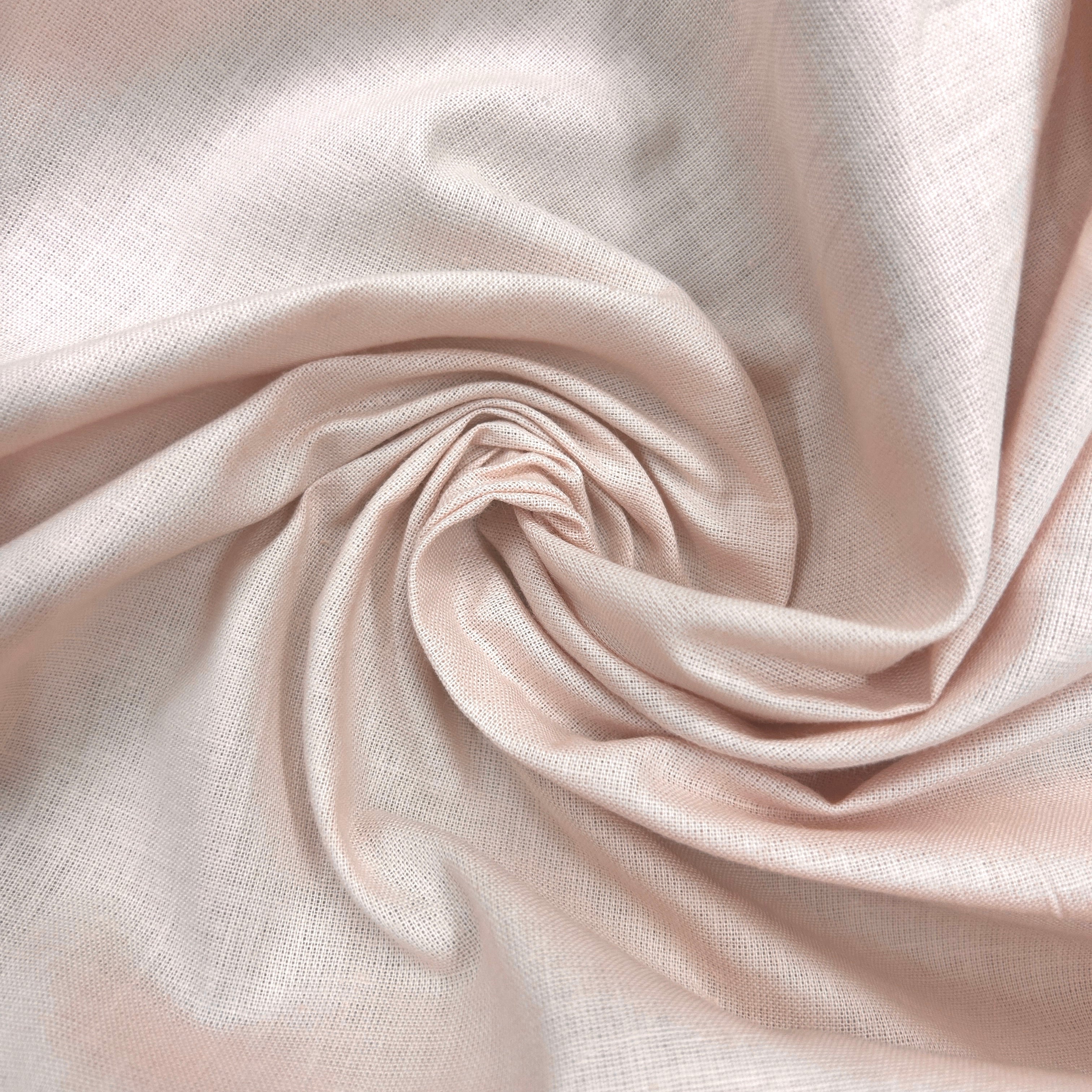 A close-up of draped light blush pink fabric arranged in a spiral, showing a soft woven texture and subtle sheen.