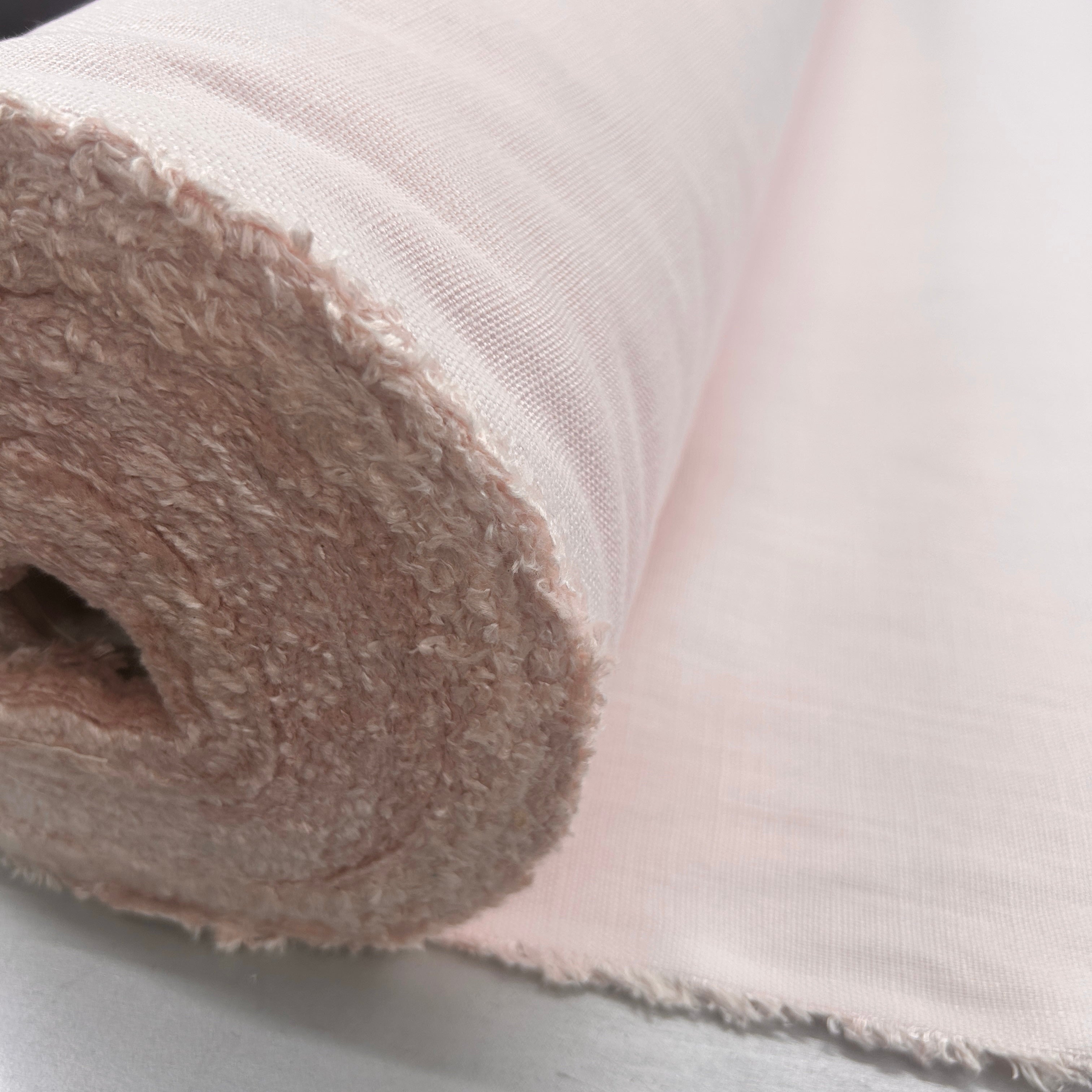A close-up of a roll of light pink woven fabric, showing both the textured looped backing and the smooth woven front side.