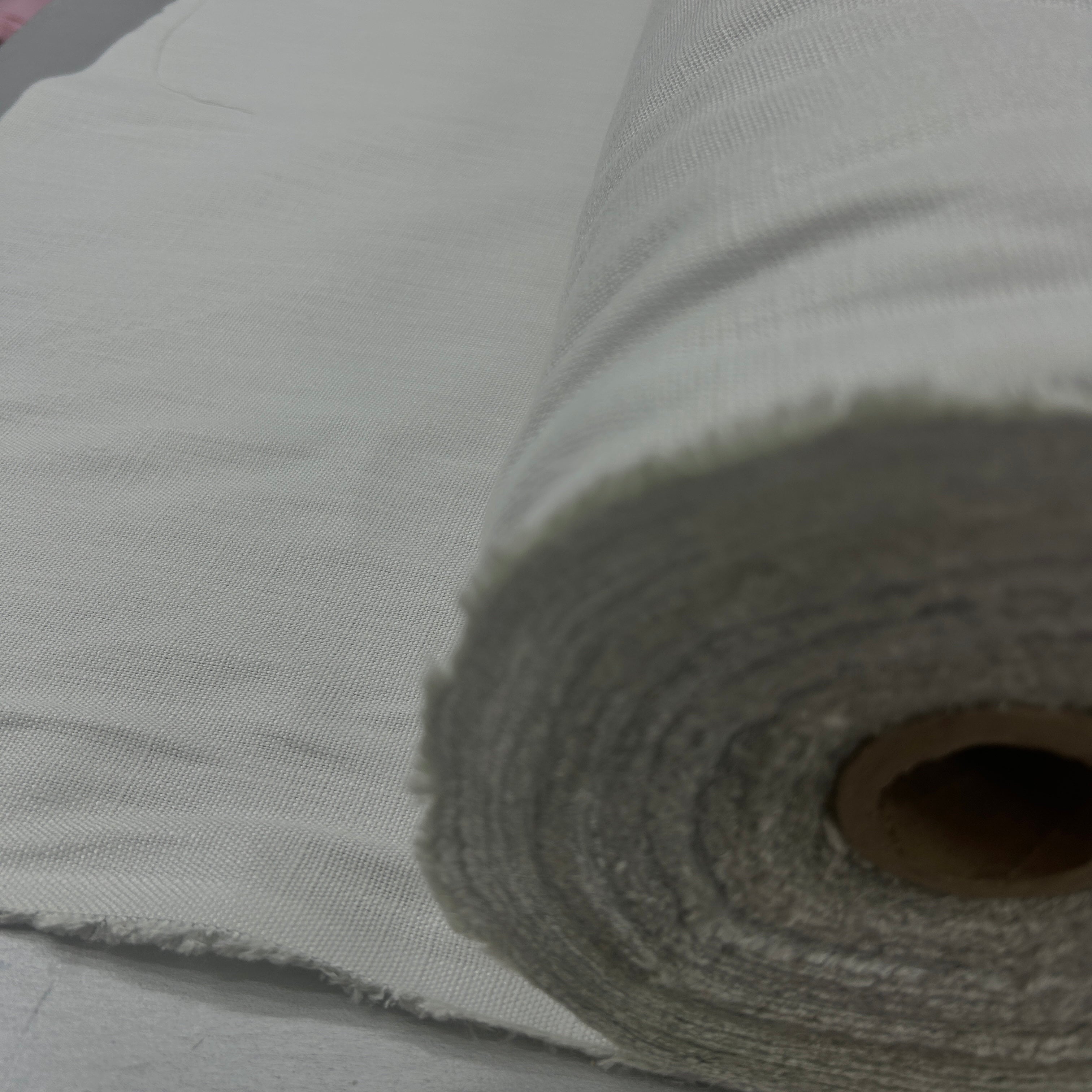 A close-up of a rolled piece of light gray woven fabric or canvas material, showing the textured weave and frayed edges, with a cardboard core visible inside the roll.