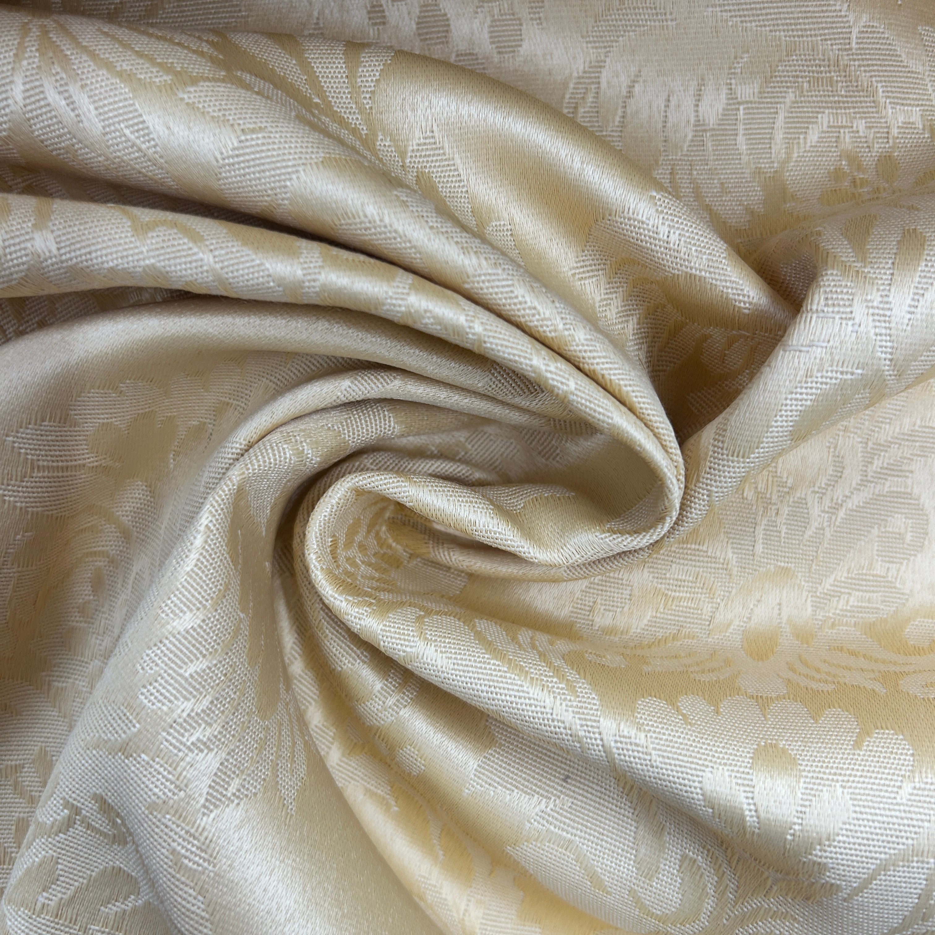 A close-up of draped champagne-colored fabric with a subtle woven floral damask pattern.