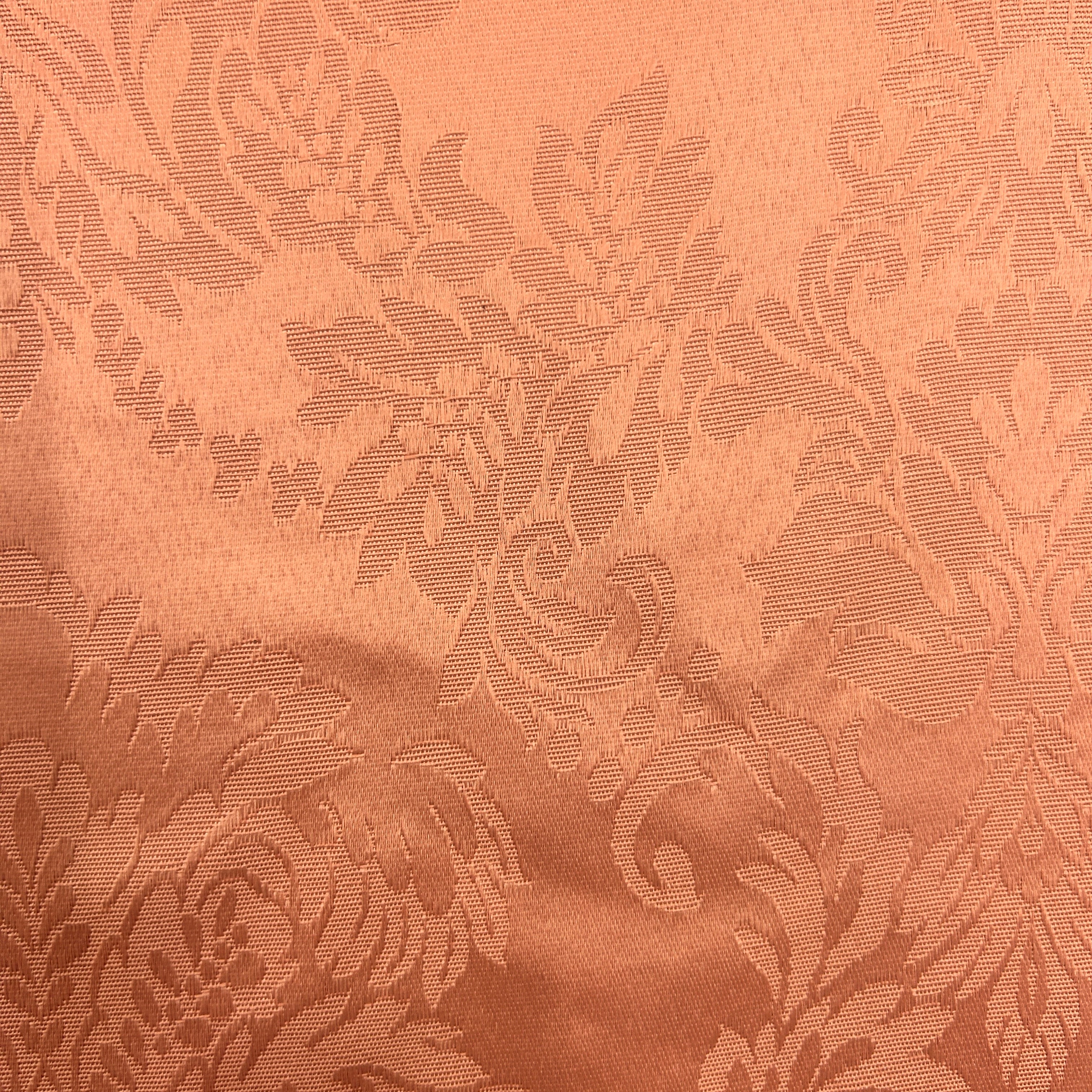 A close-up of a peach-colored fabric with a woven damask floral pattern.
