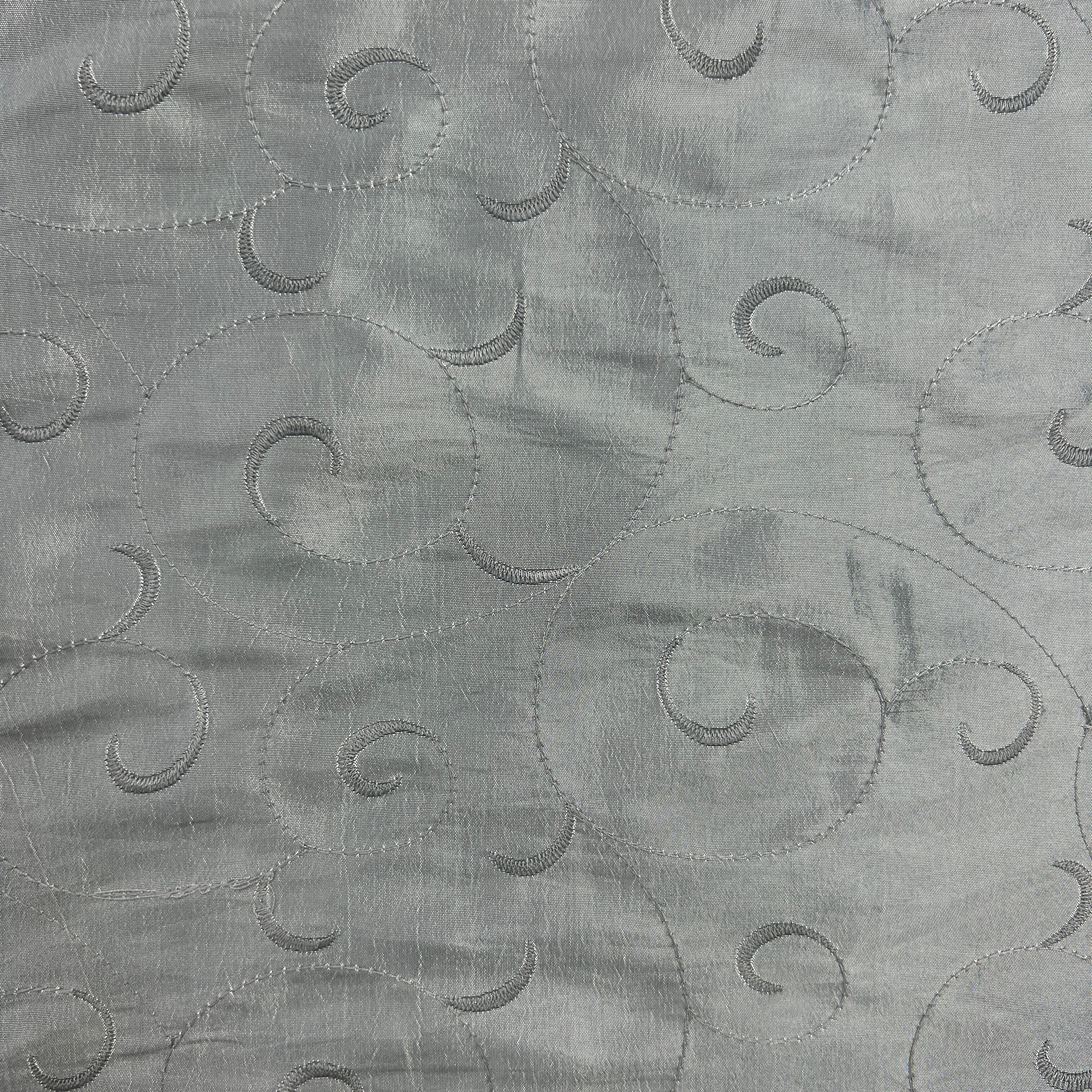 A close-up of a light gray fabric with an embroidered swirling cloud-like pattern.