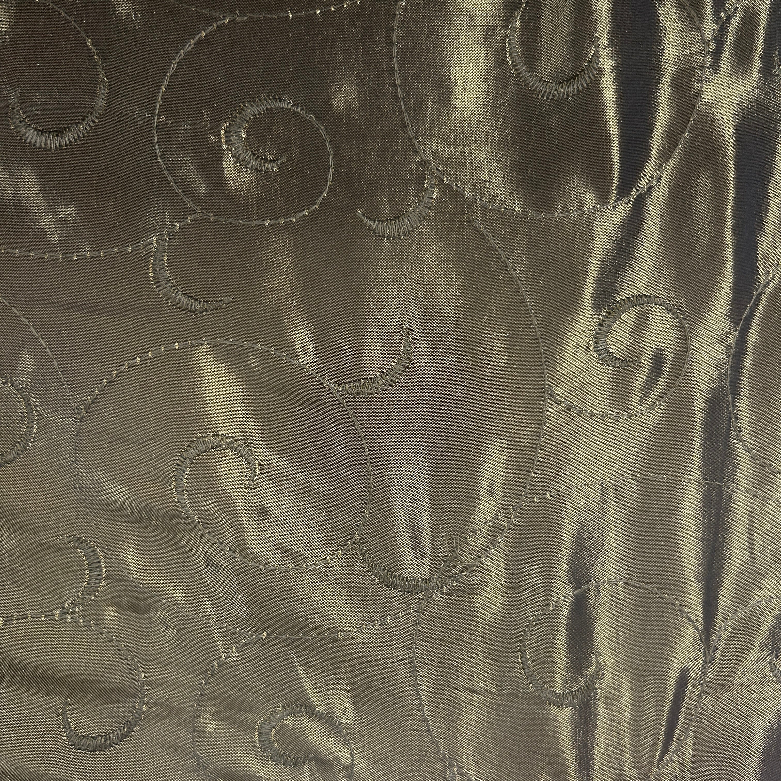 A close-up of a metallic taupe fabric with a satin-like sheen and an embroidered swirl pattern.