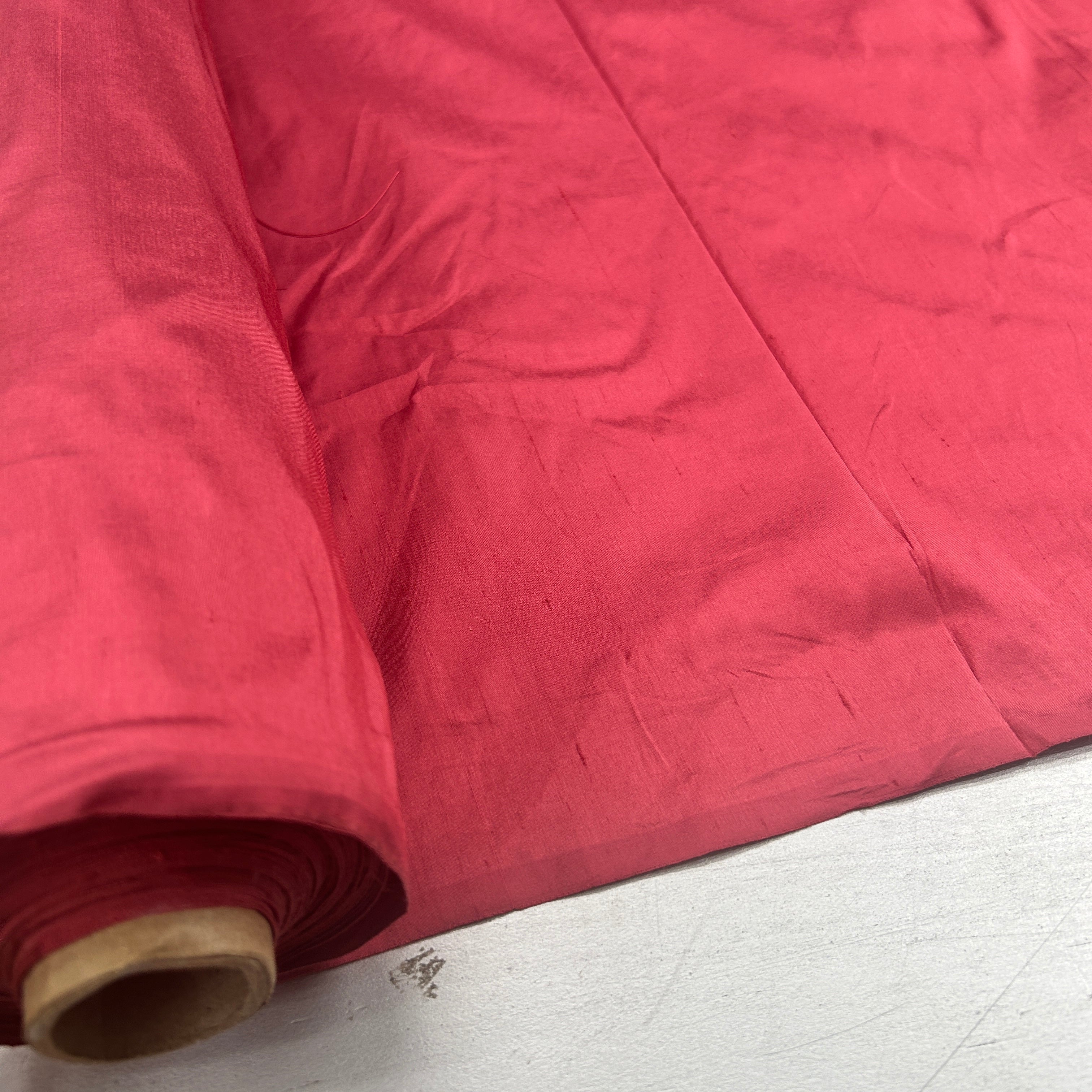 A close-up of a roll of bright pink fabric, partially unrolled to show its texture and color, resting on a light-colored surface.