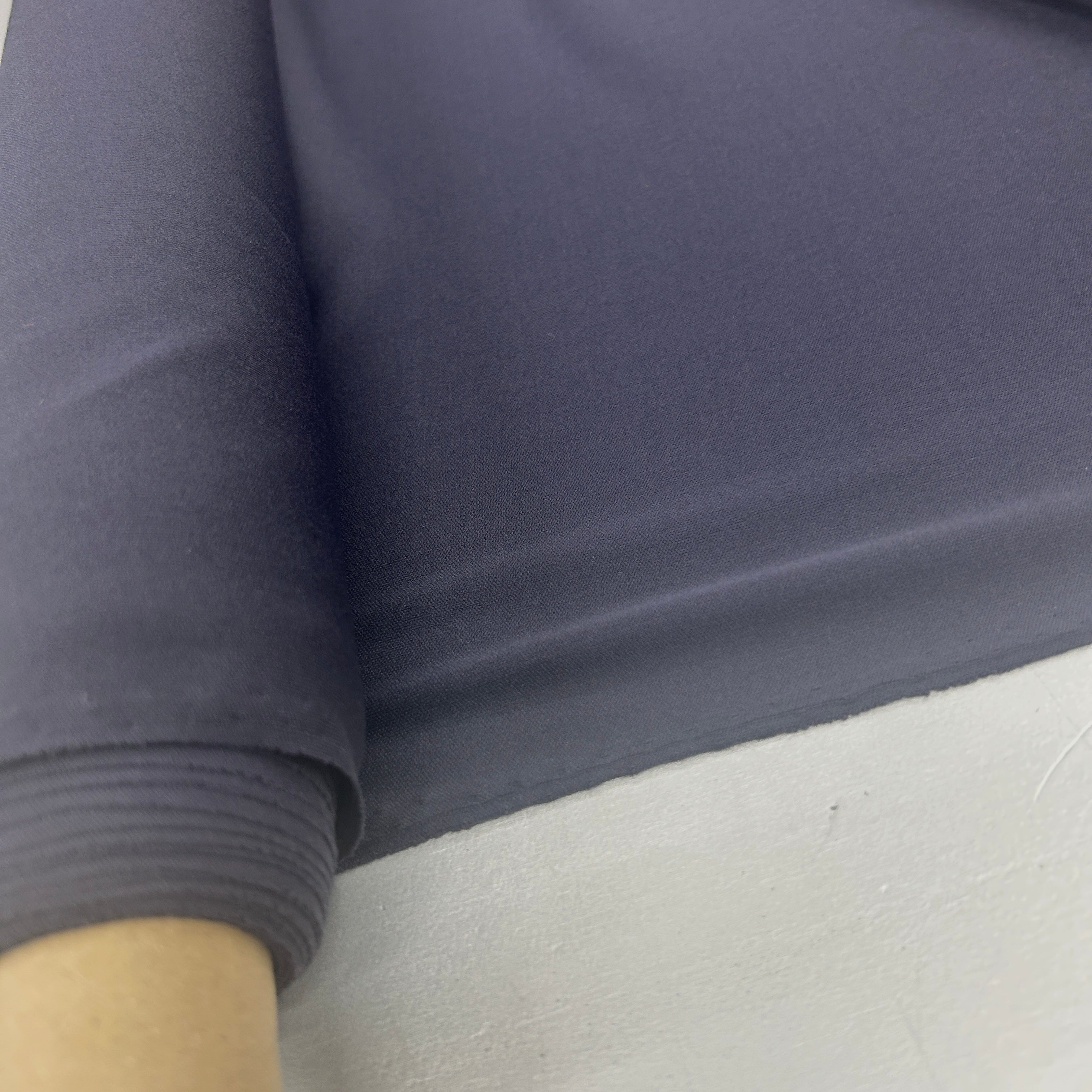 A close-up of dark slate blue-gray fabric draped over a light gray surface, with a rolled section showing the material's texture and color.