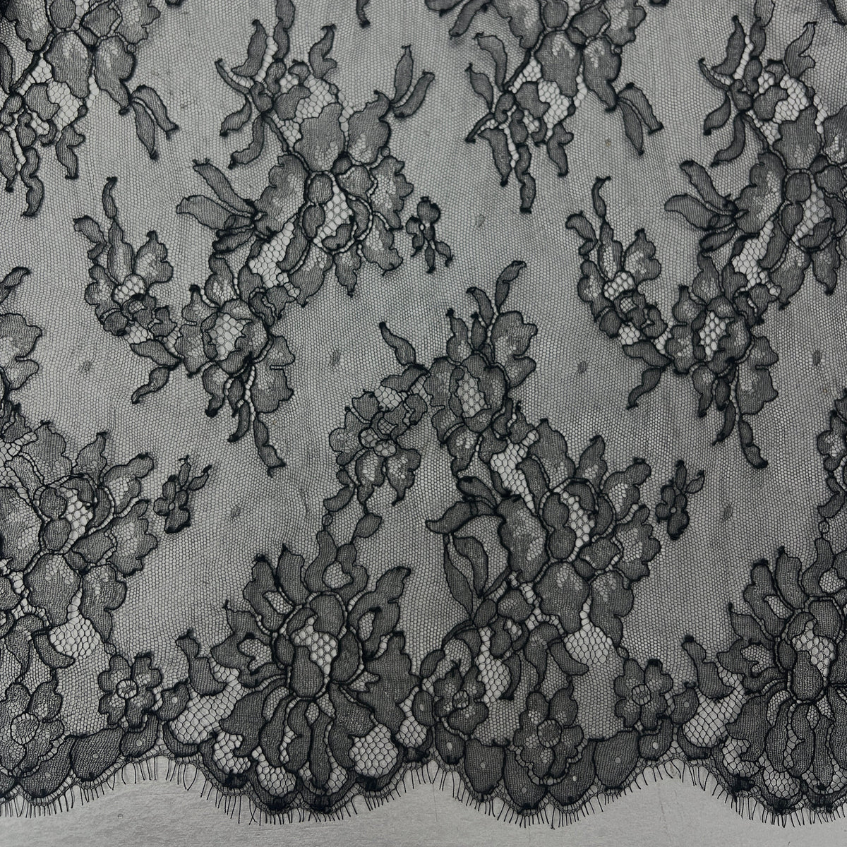 Black floral lace fabric with a scalloped edge, shown in a close-up texture view.