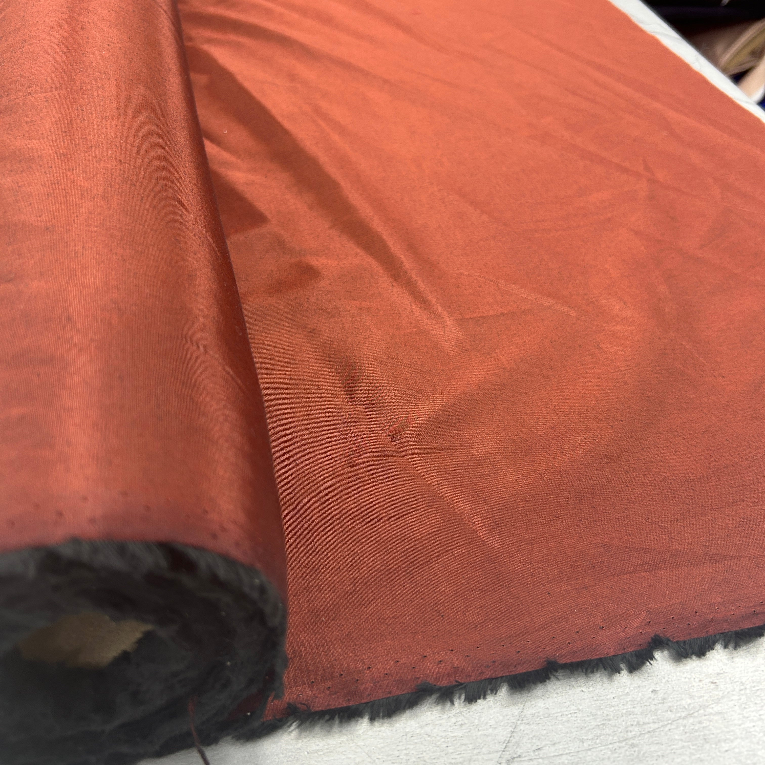 A close-up of rust-orange fabric, partially rolled, showing its woven texture and a dark backing.