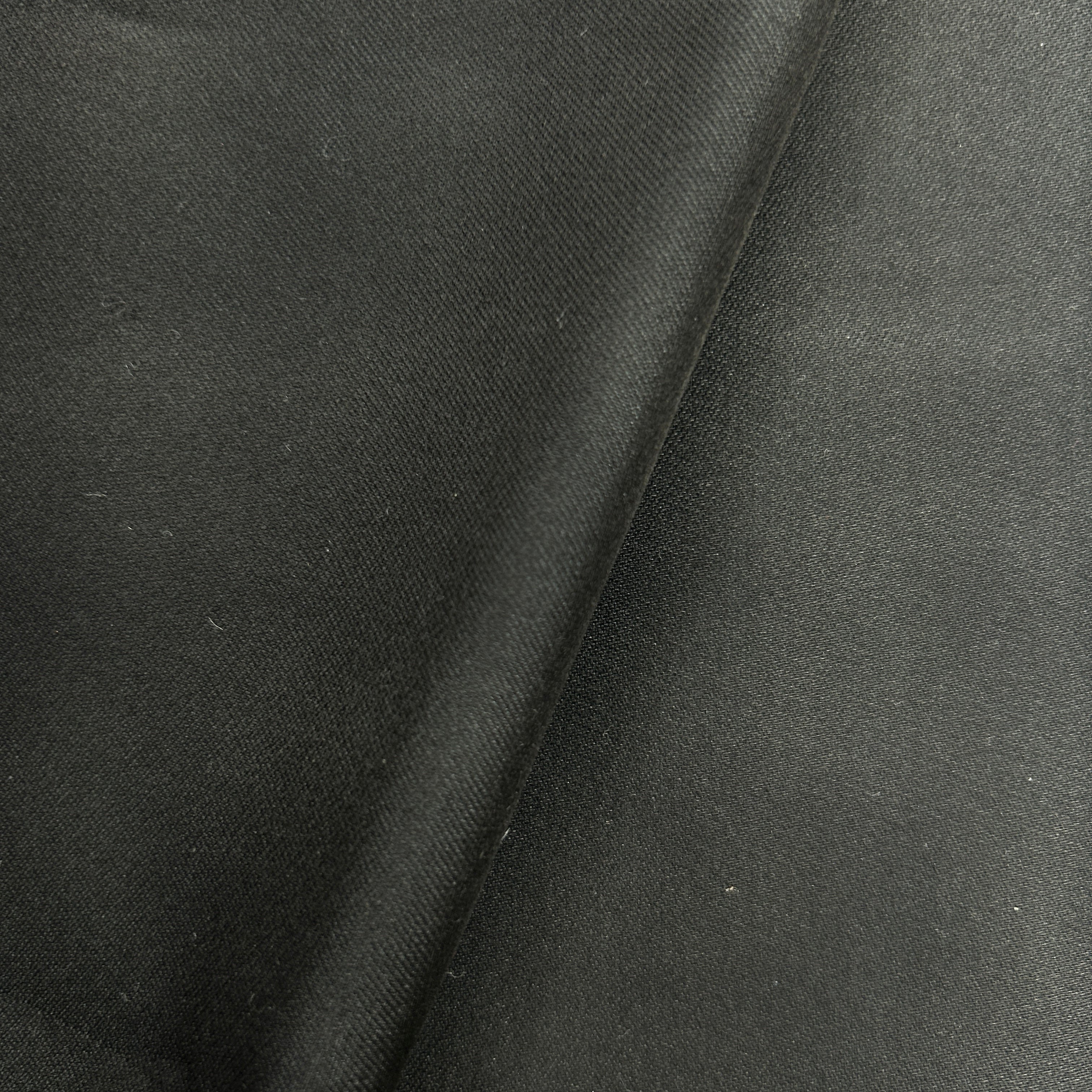 A close-up of dark charcoal gray fabric with a diagonal fold showing the texture and weave.