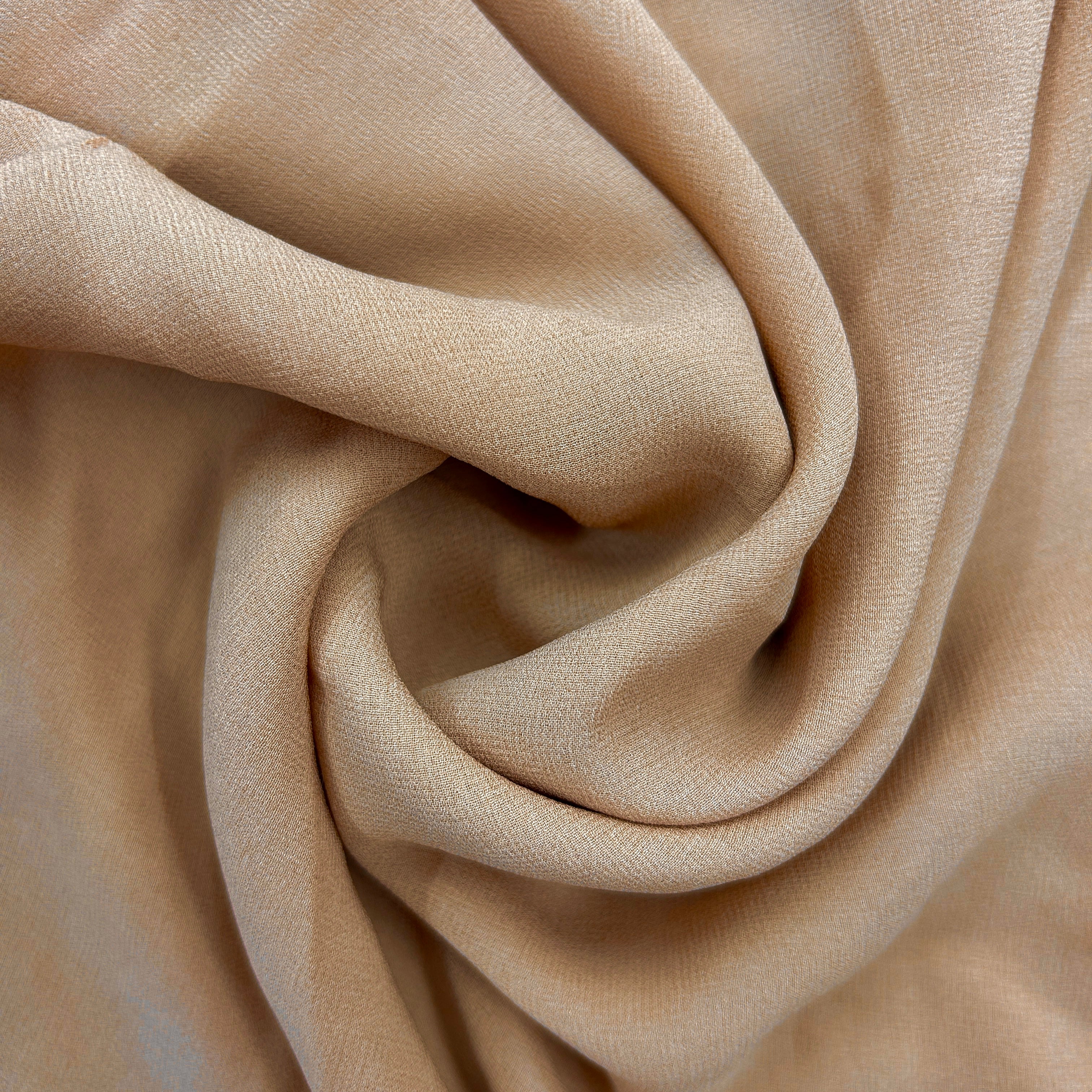 A close-up of draped beige fabric with a soft, slightly sheer texture, arranged in elegant folds.