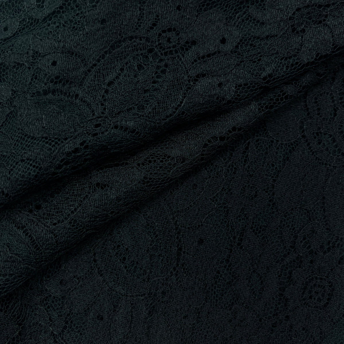 Close-up of black lace fabric with an intricate floral and scroll pattern, draped diagonally across the frame.