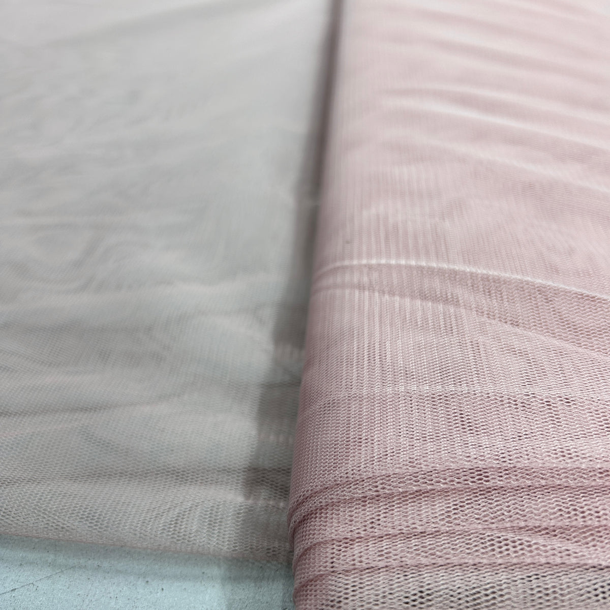 A close-up of sheer mesh fabric in two colors: a light gray on the left and a dusty pink on the right, folded over to show texture and transparency.