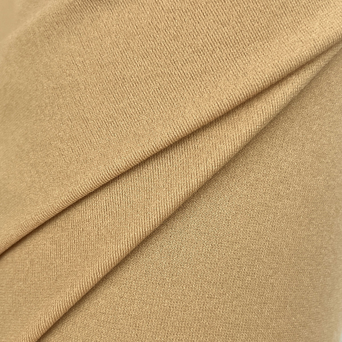 A close-up of draped tan fabric with a fine ribbed texture, showing soft folds and shadows.