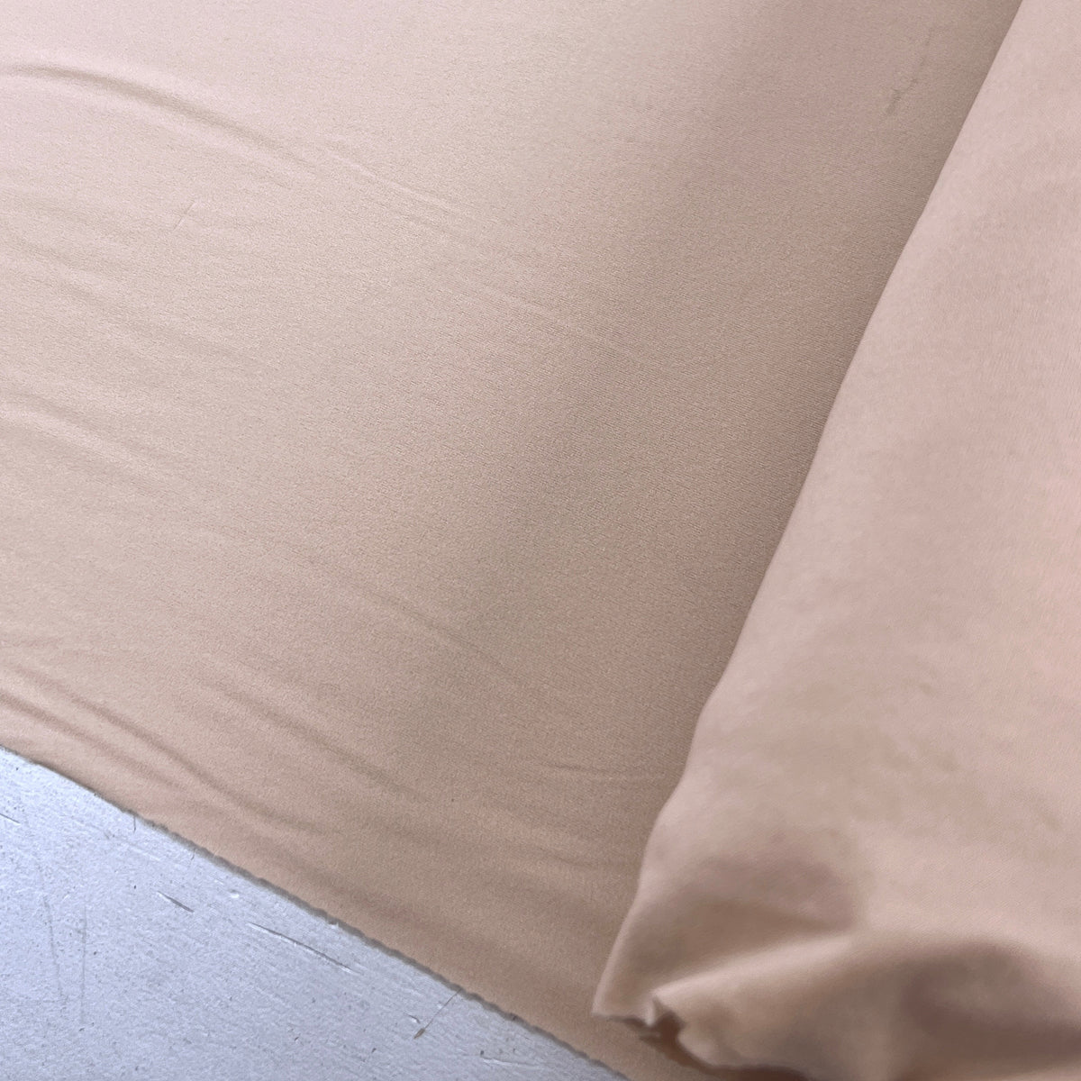 A close-up of a light beige or nude-colored fabric, showing its soft texture and folds, draped over a white surface.