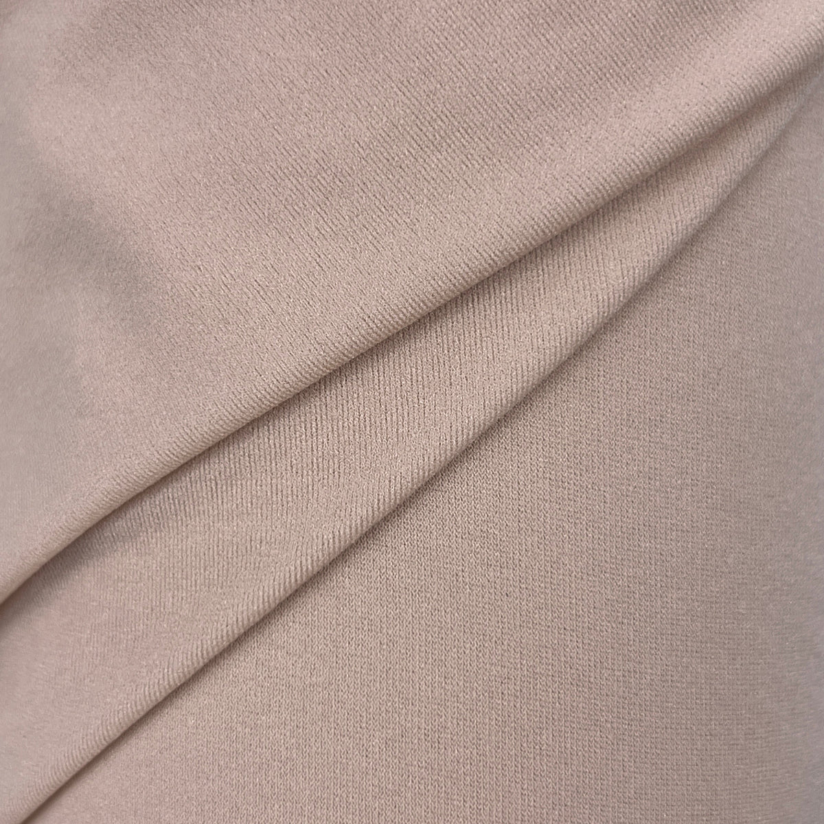A close-up of draped beige fabric with a fine knit texture, showing soft folds and shadows.