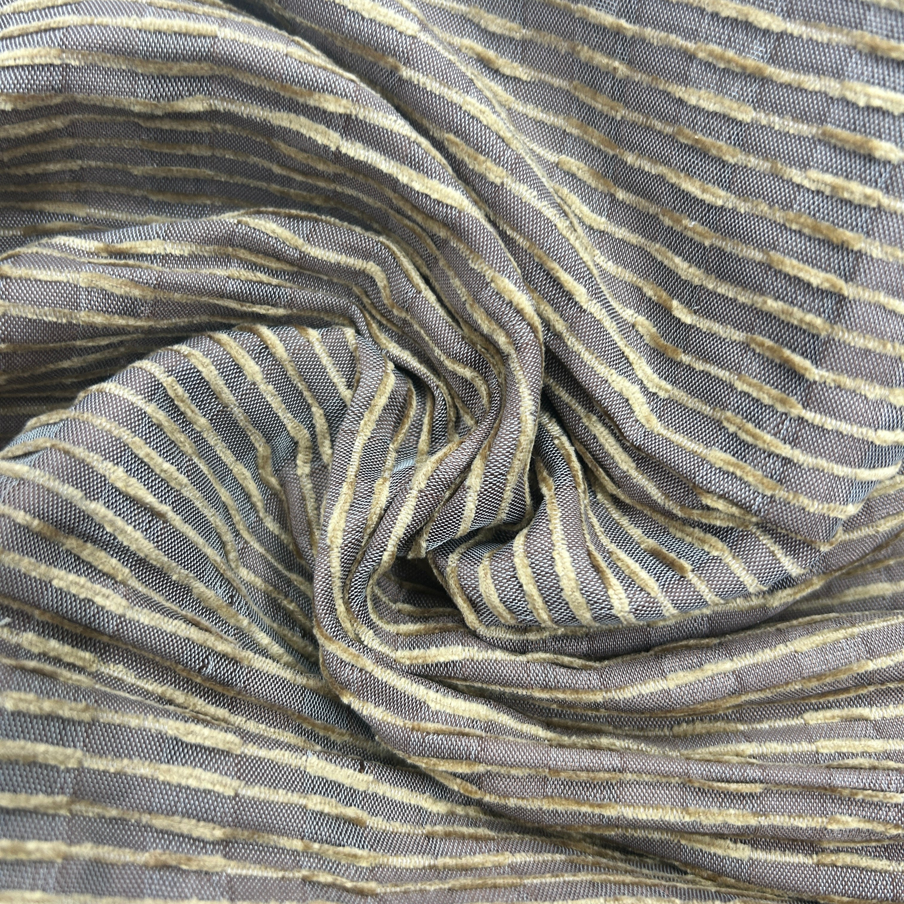 A close-up of draped fabric with a gray base and thin, slightly distressed vertical stripes in beige and muted gold.