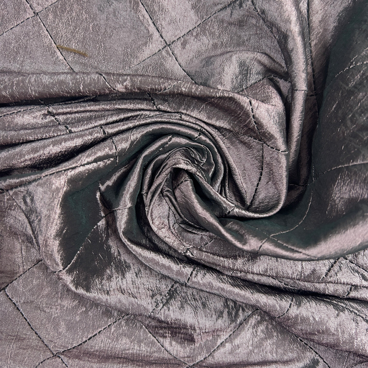 A close-up of draped metallic fabric with a quilted diamond pattern, shown in a spiral fold to highlight its texture and sheen.