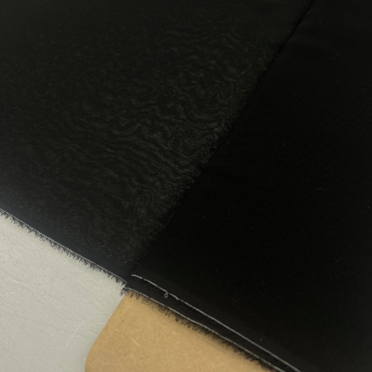 A close-up of a black textured material, likely leather or faux leather, folded over to show its surface texture and edge, with a light-colored surface visible underneath.