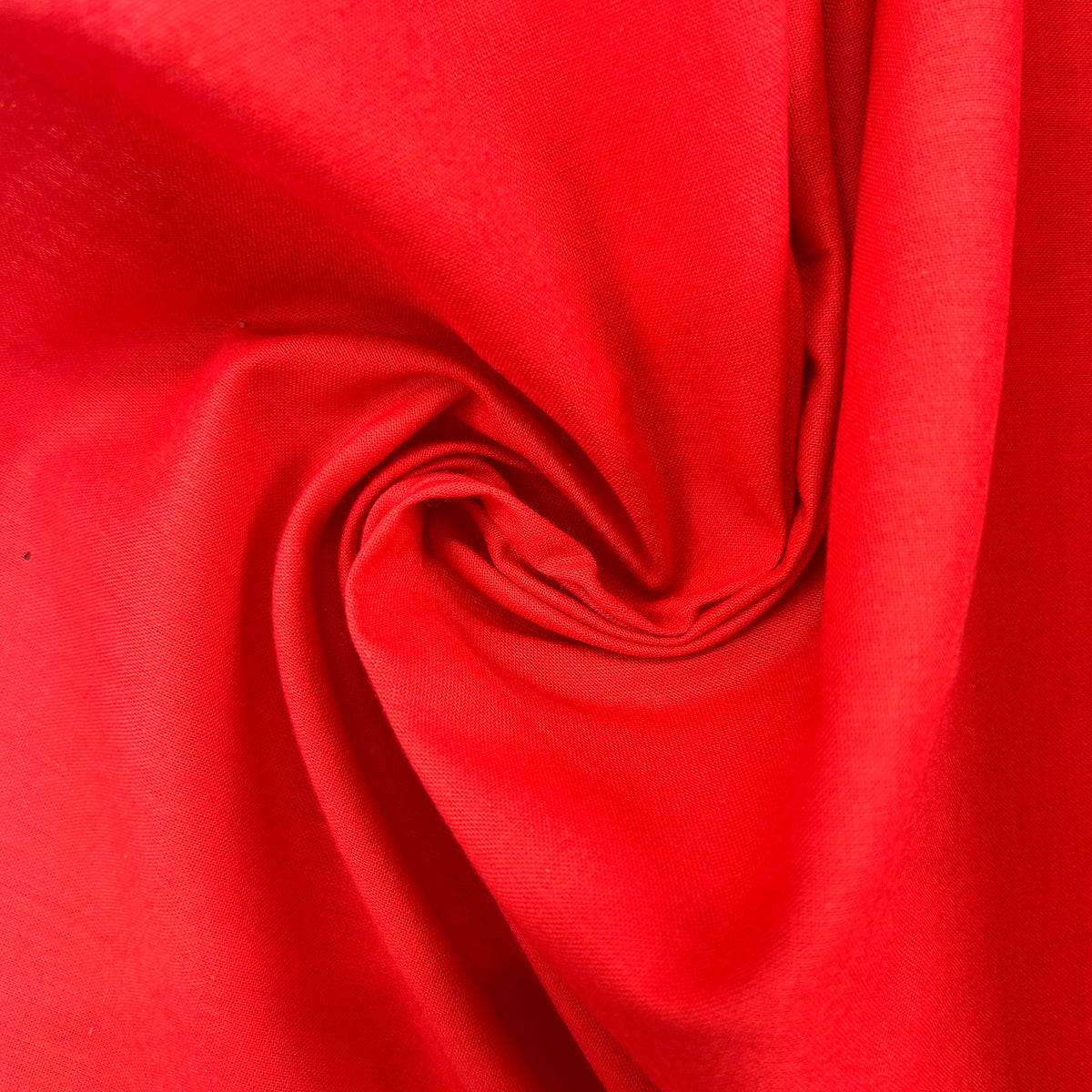 A close-up of bright red fabric arranged in a spiral drape, showing the material texture and color.