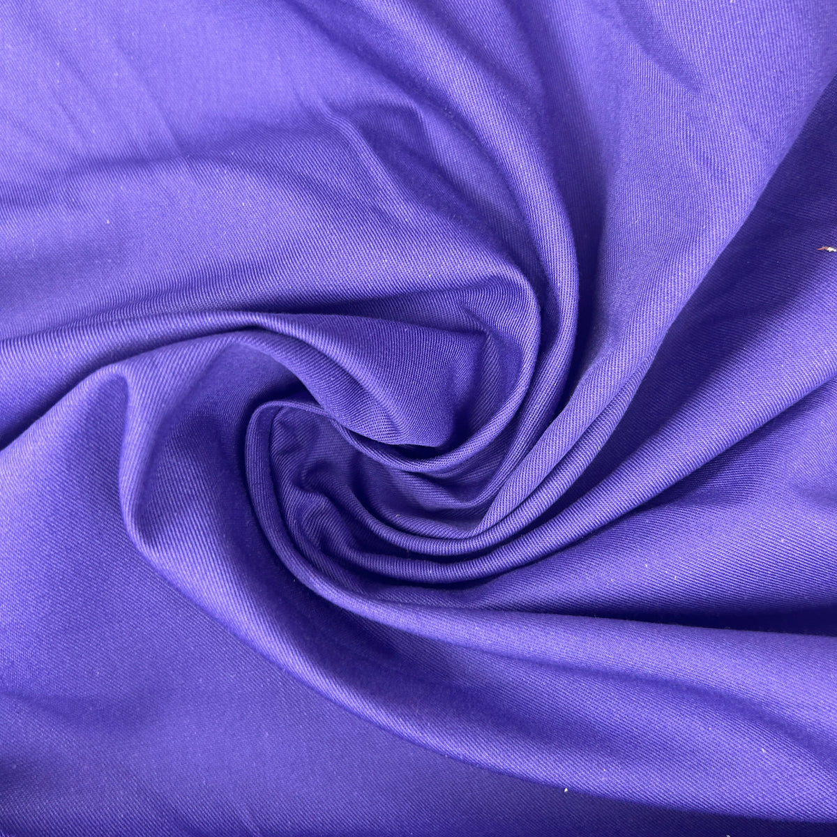 A close-up of purple fabric arranged in a spiral drape, showing the material texture and color.