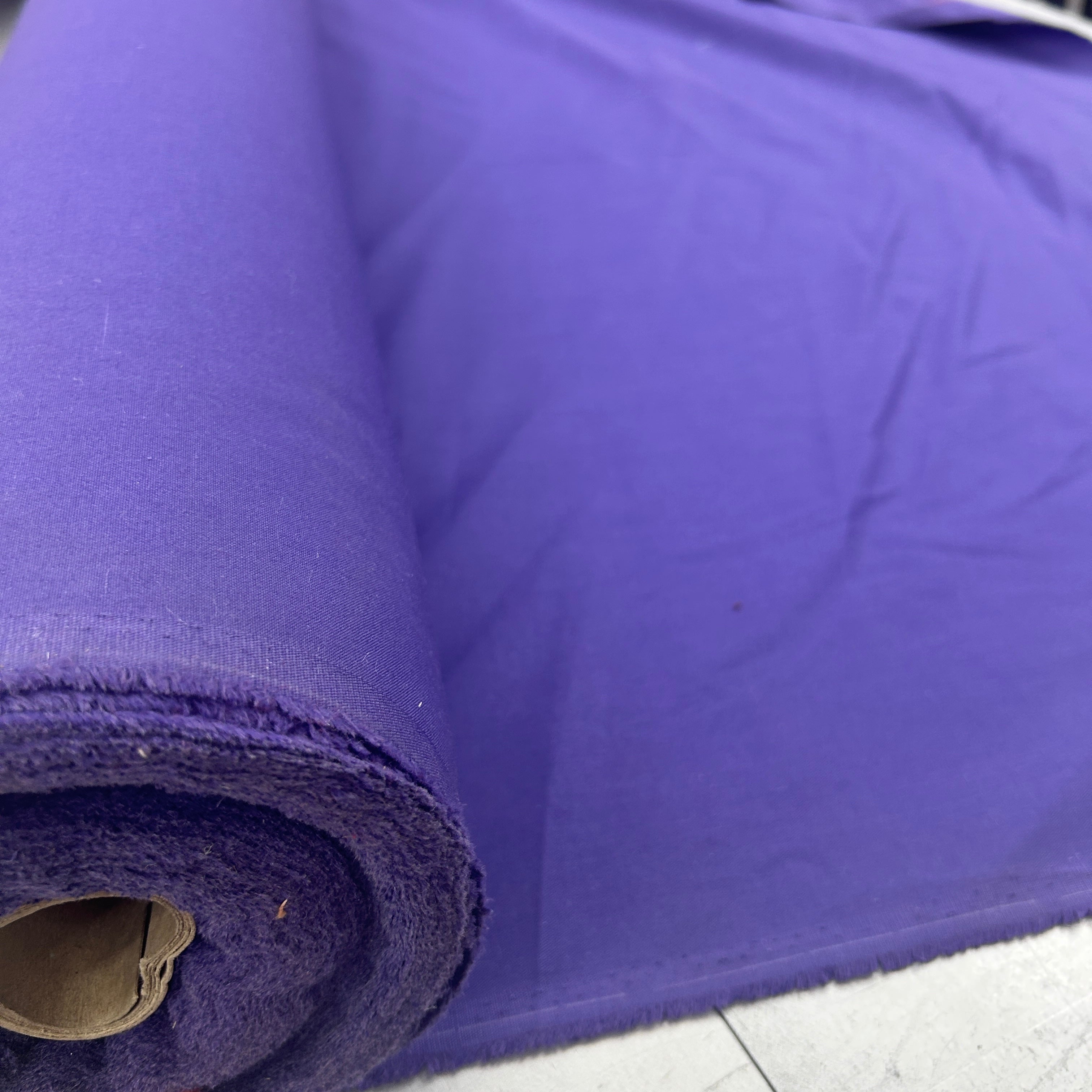 A roll of solid purple fabric, shown partially unrolled to display its texture and color.