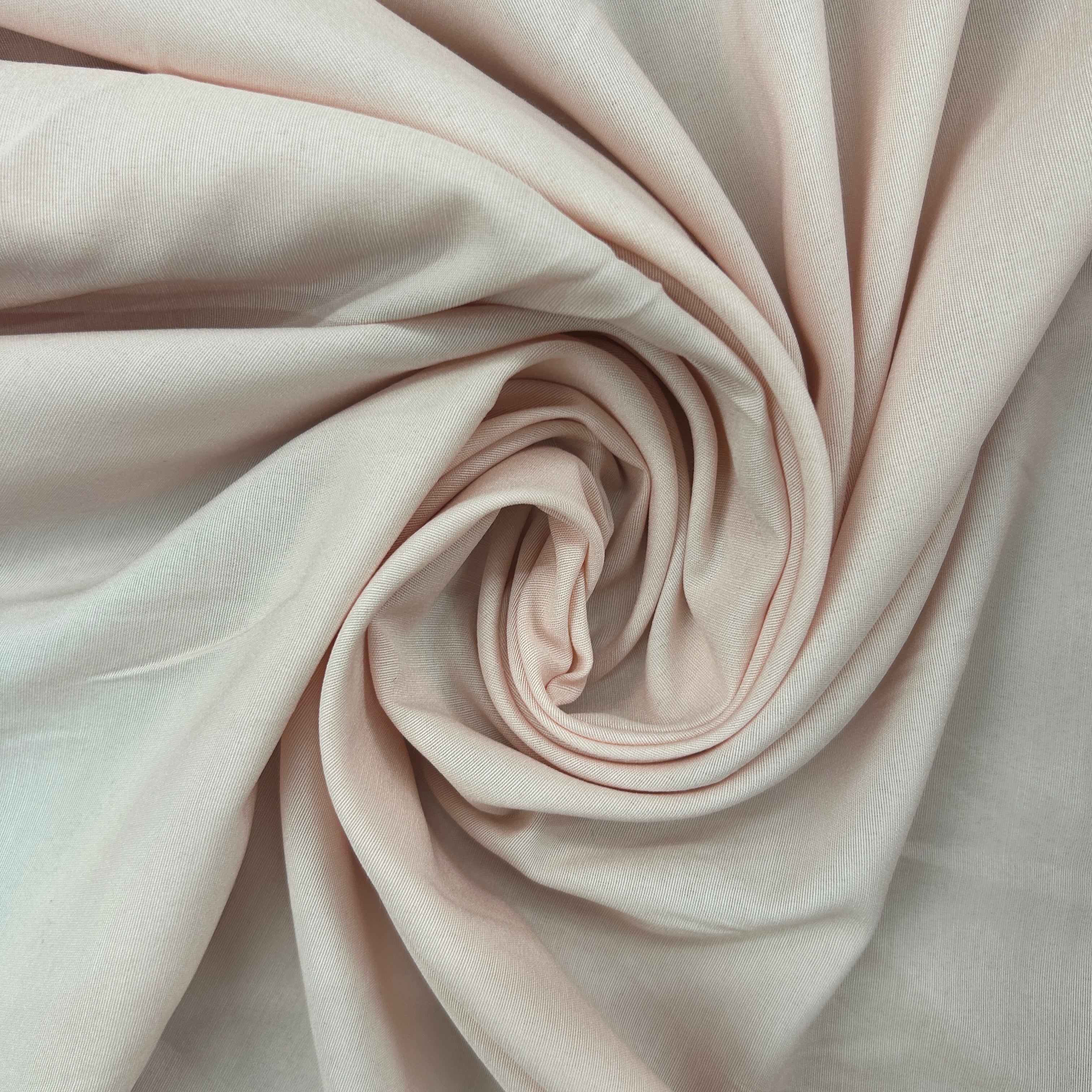 A close-up of soft blush pink fabric arranged in a spiral drape, showing the material's smooth texture and light color.