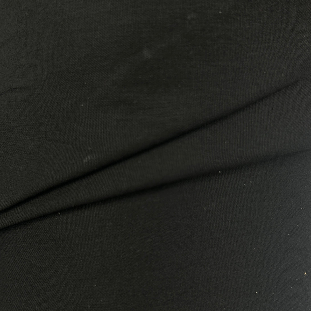 A close-up of black fabric with a fine knit texture and a diagonal fold running across the center.