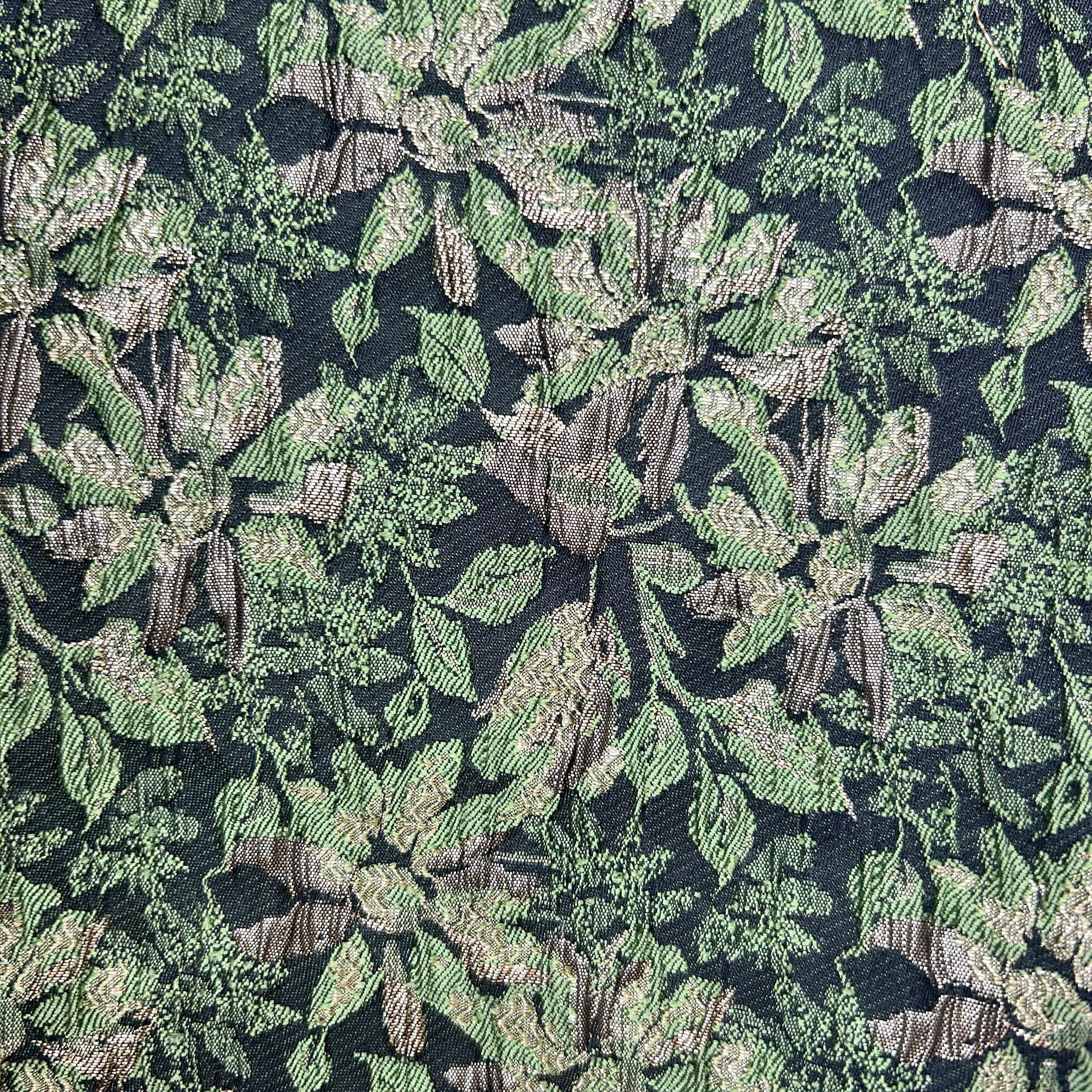 Close-up of green floral brocade upholstery fabric with intricate leaf and flower patterns.